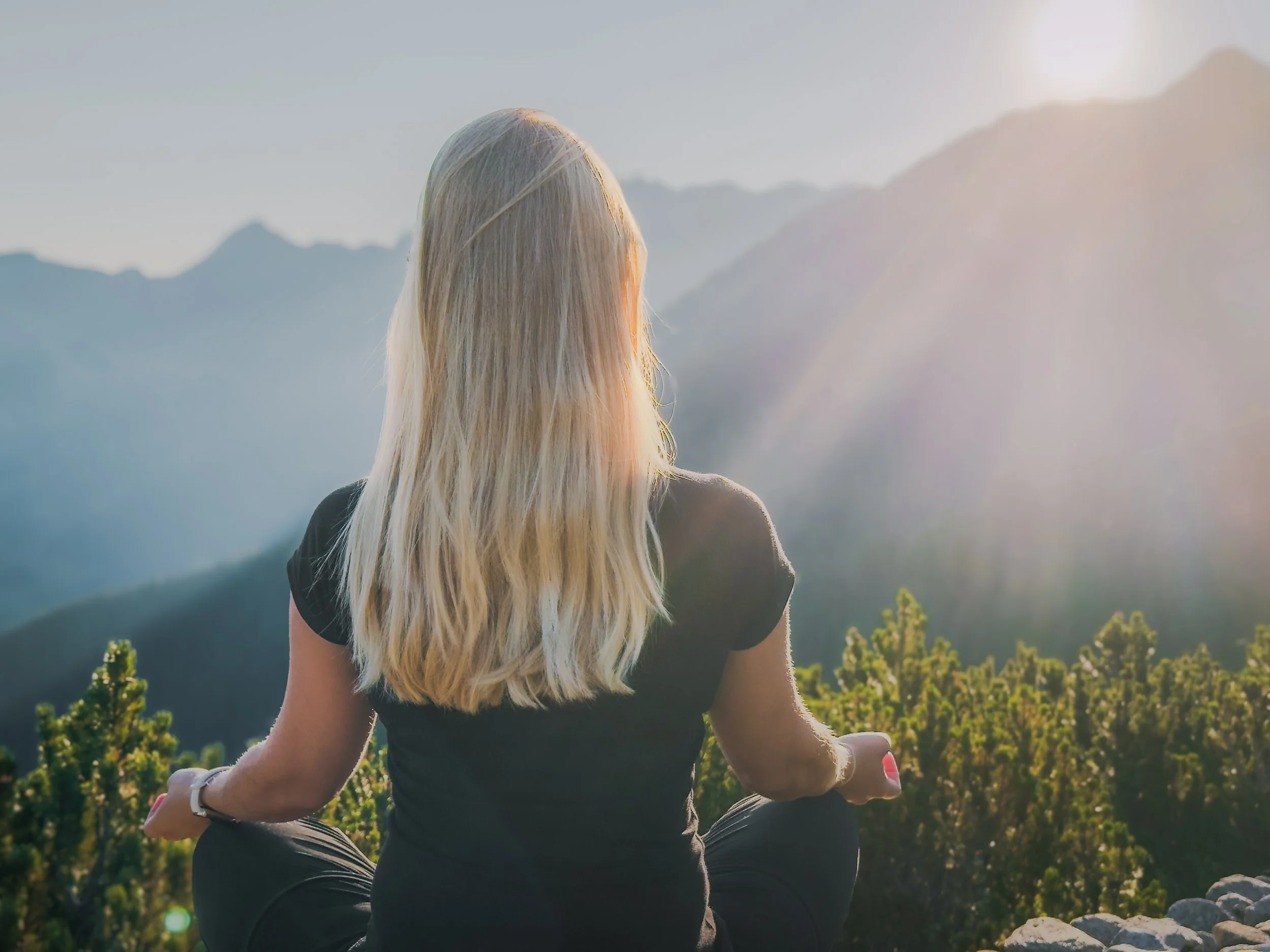 Frau meditiert im Sitzen auf einem Felsen in den Bergen bei Sonnenaufgang.