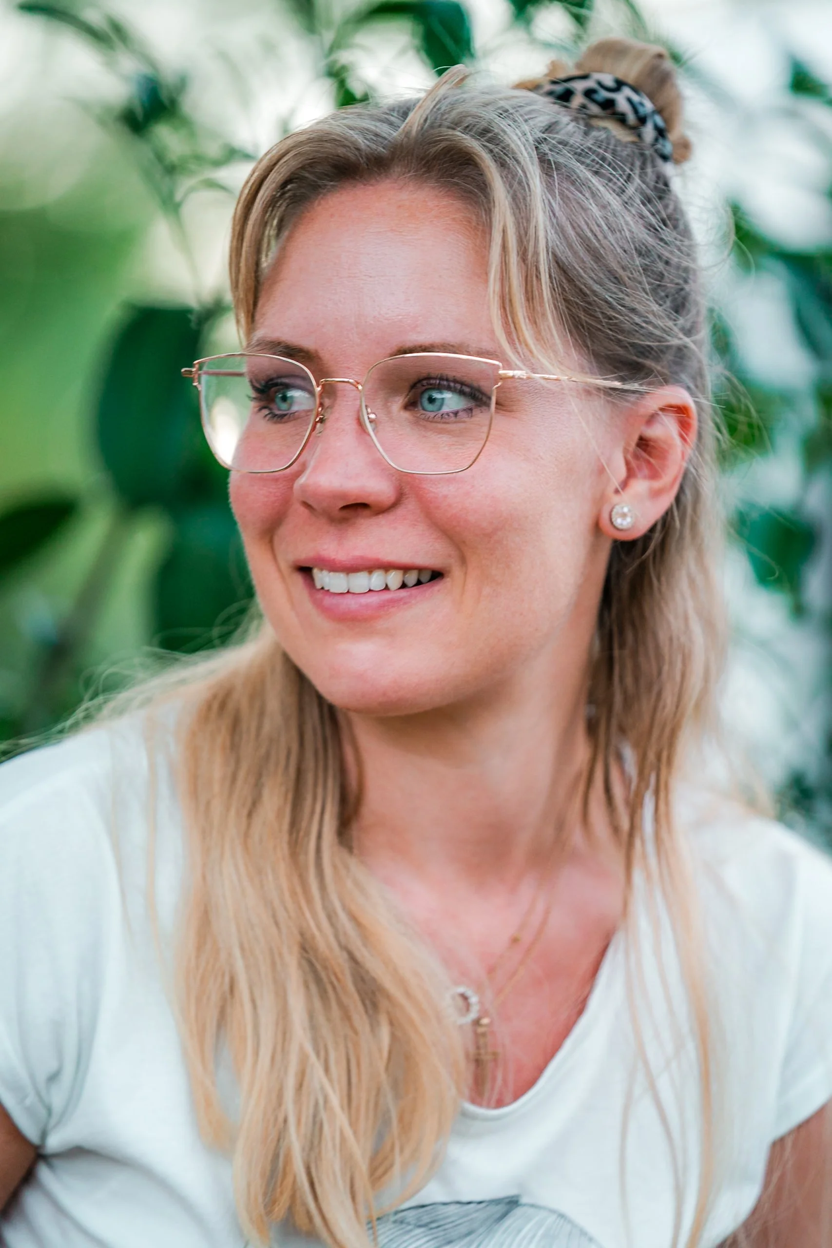 Ein lachendes Mädchen mit blonden Haaren, Brille und Ohrringen, im Grünen.