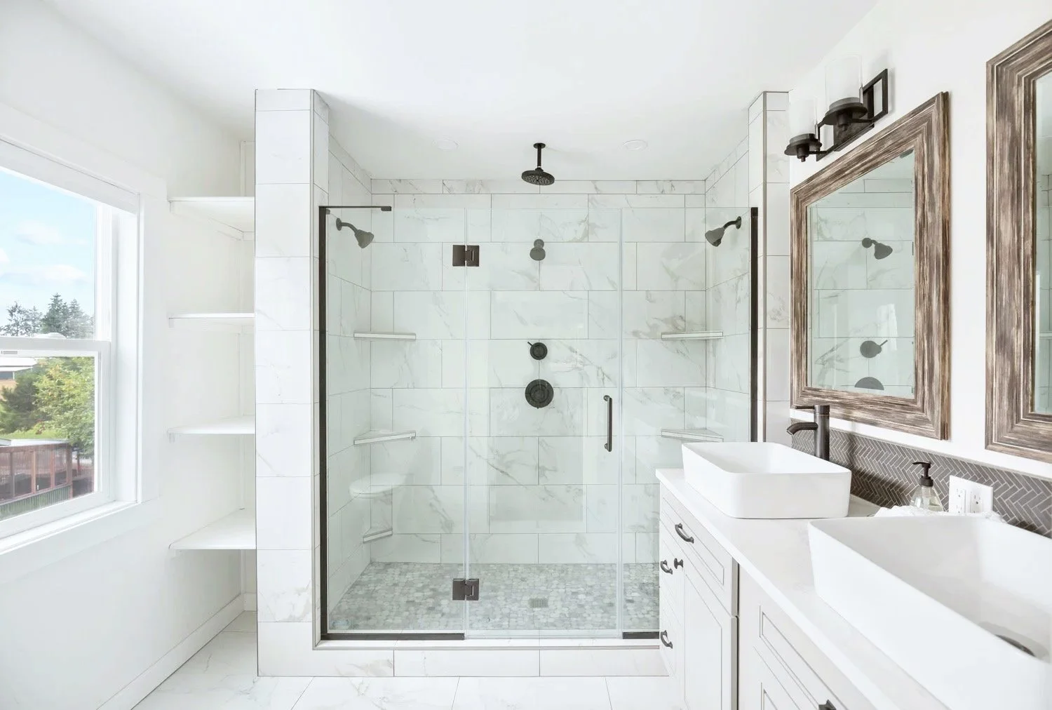 Modern bathroom with a glass-enclosed shower, white marble walls, wooden framed mirrors, and dual vessel sinks.