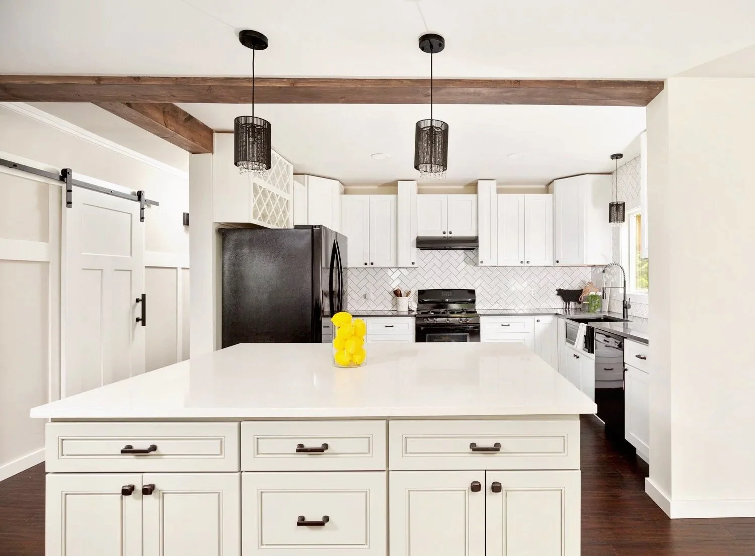 Modern kitchen with white cabinets, black appliances, and a large white island counter with a jar of yellow lemons.