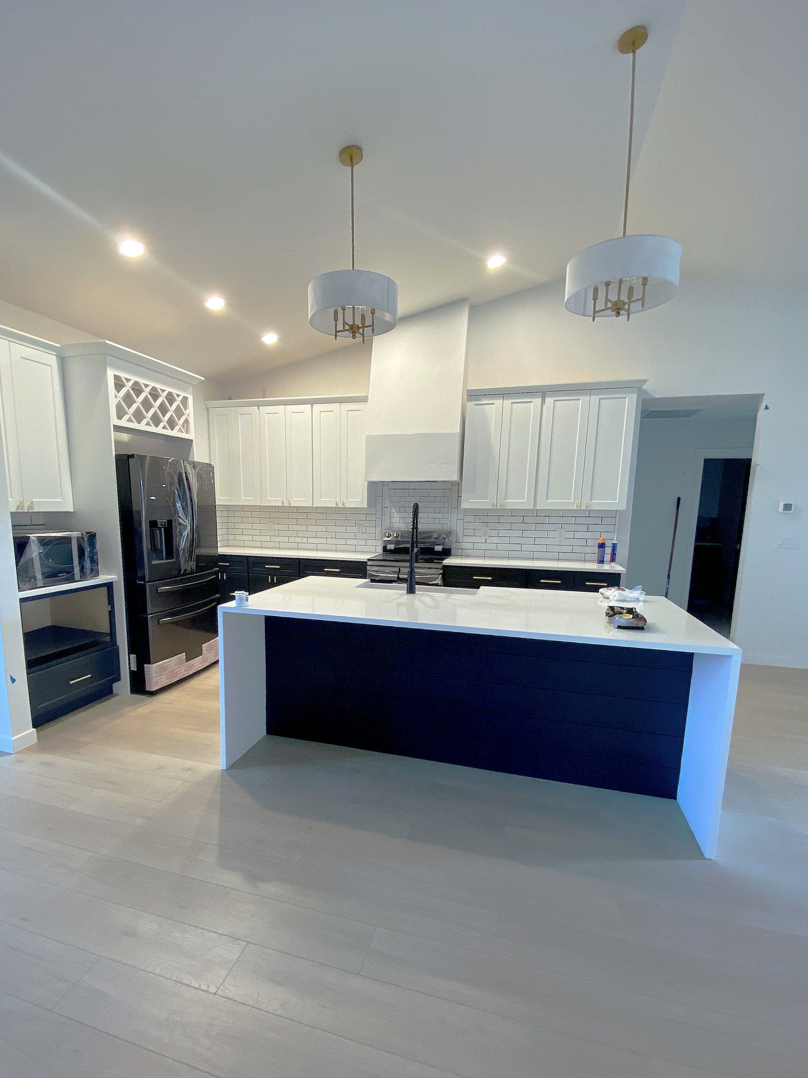 Modern kitchen with white cabinets, black lower cabinets, a white island with a black base, stainless steel appliances, white tile backsplash, and two hanging light fixtures.