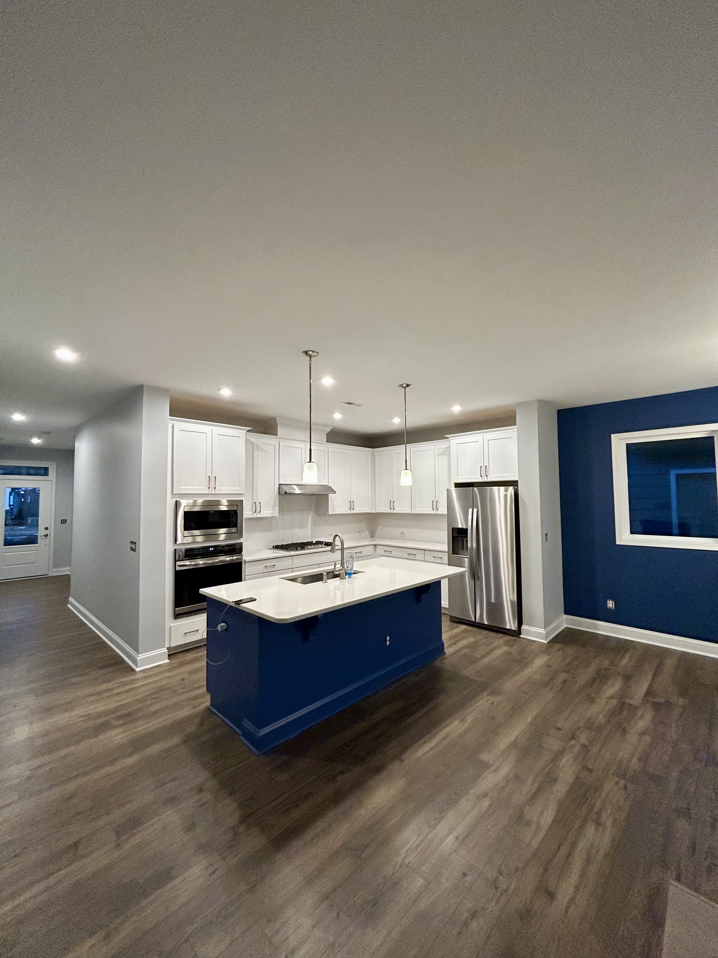 Modern kitchen with a blue island, white cabinets, stainless steel appliances, and wood flooring.