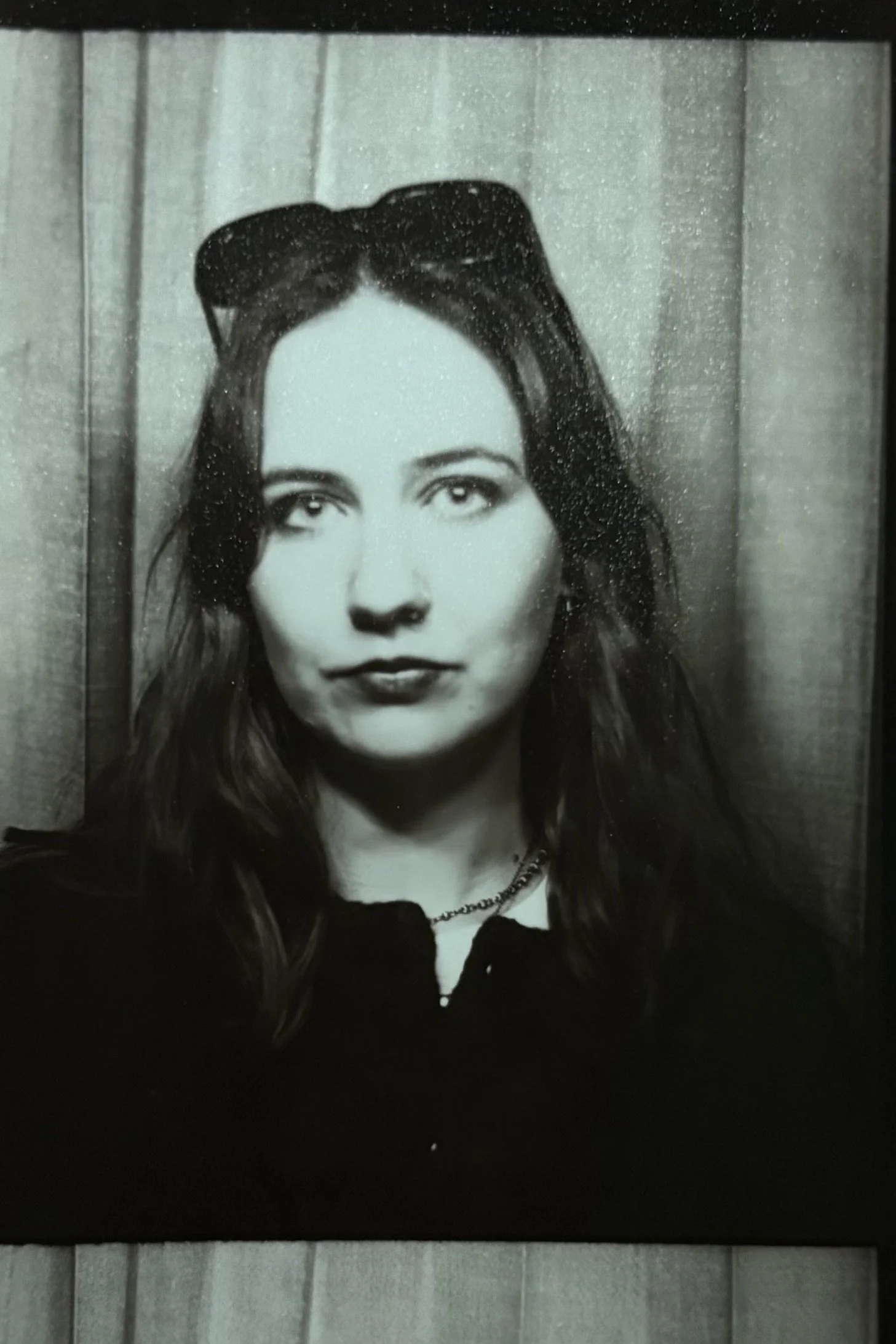 Black and white portrait of a woman with long hair, wearing a necklace and a top with a collar, against a wooden background.