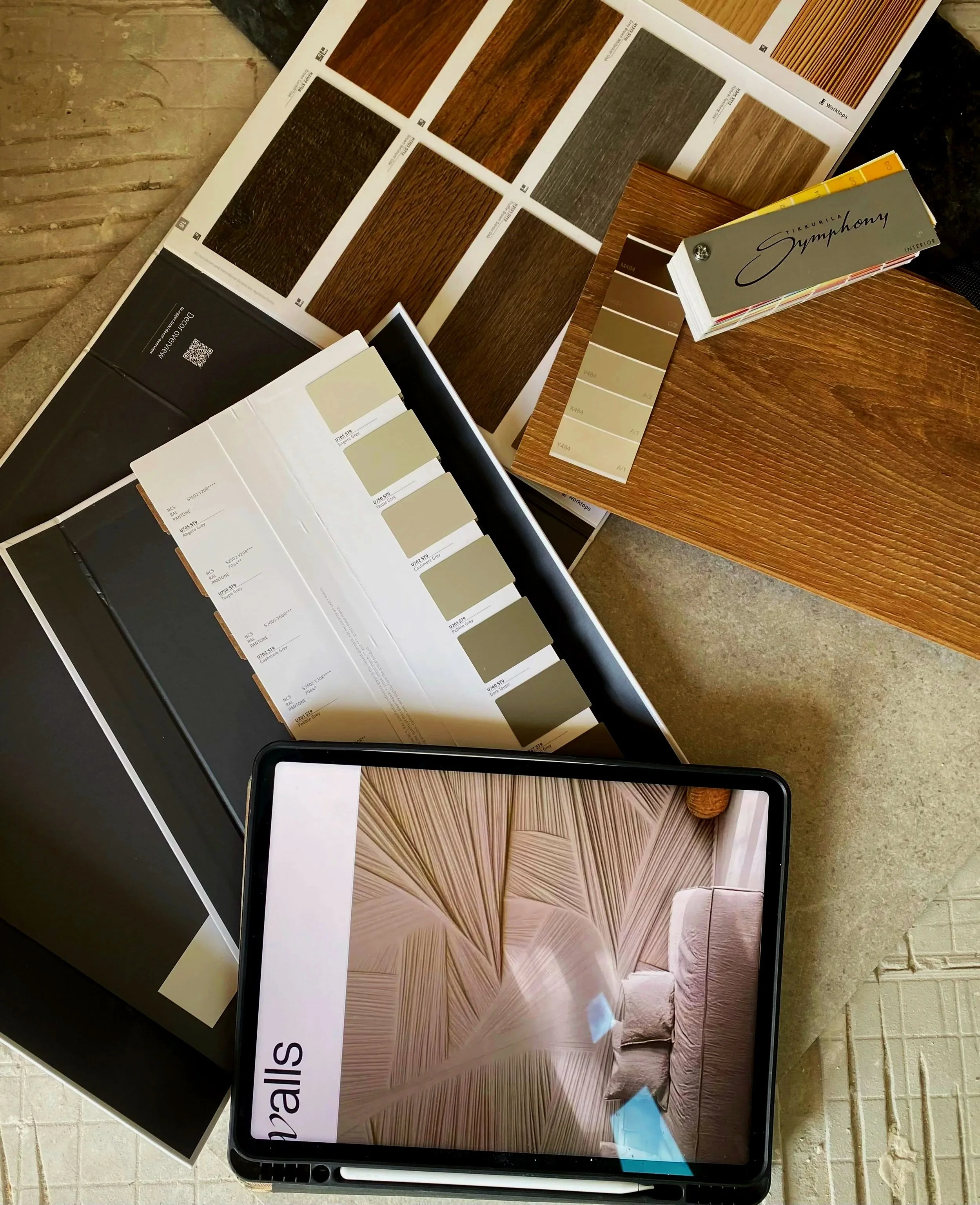 Samples of wood grain patterns and colors on display, with a booklet or catalog labeled 'Tikkurila Symphony Interior' for wood finishes, arranged on a table for selection.