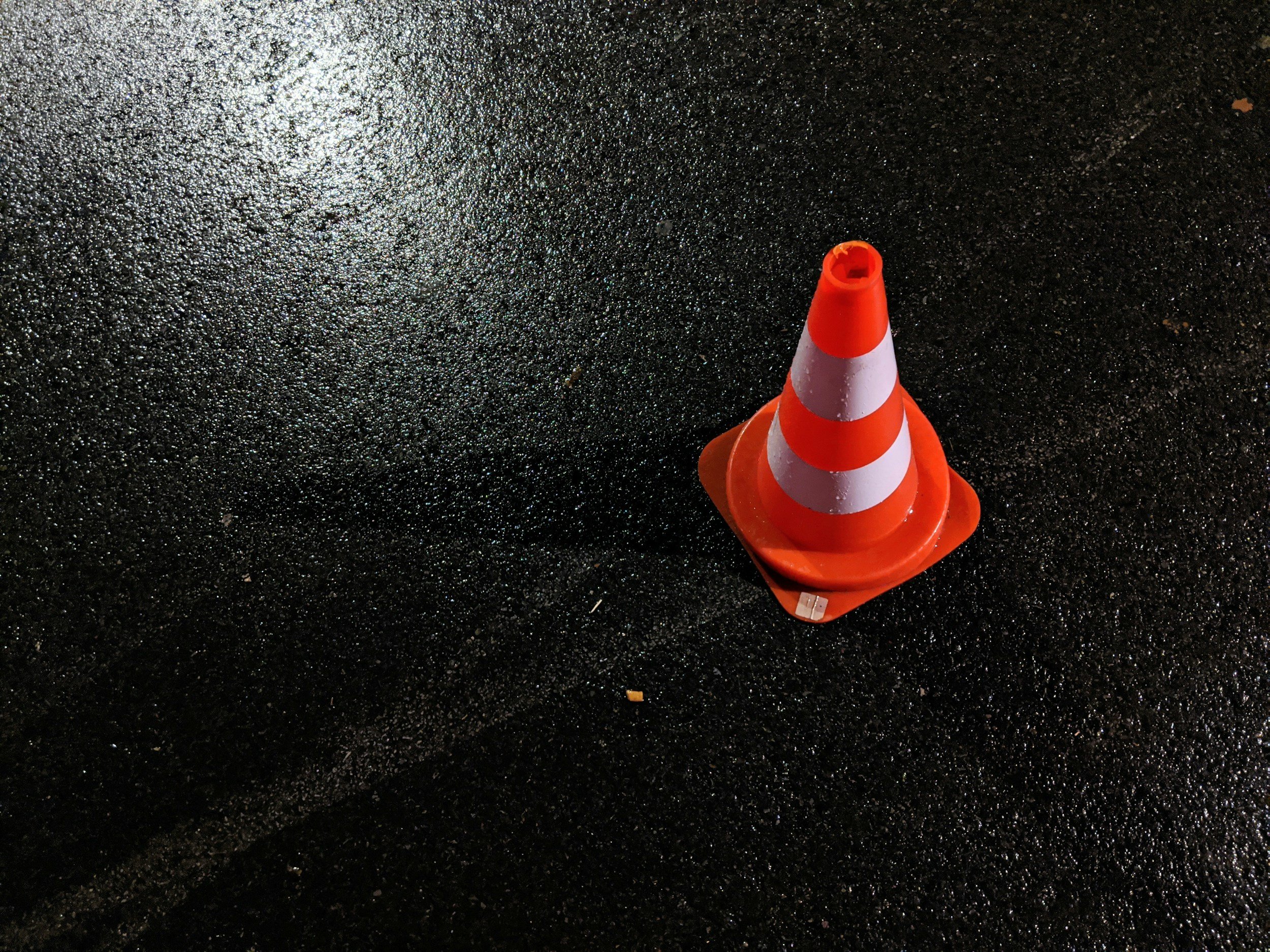 Orange and white striped traffic cone on a wet, black asphalt surface.