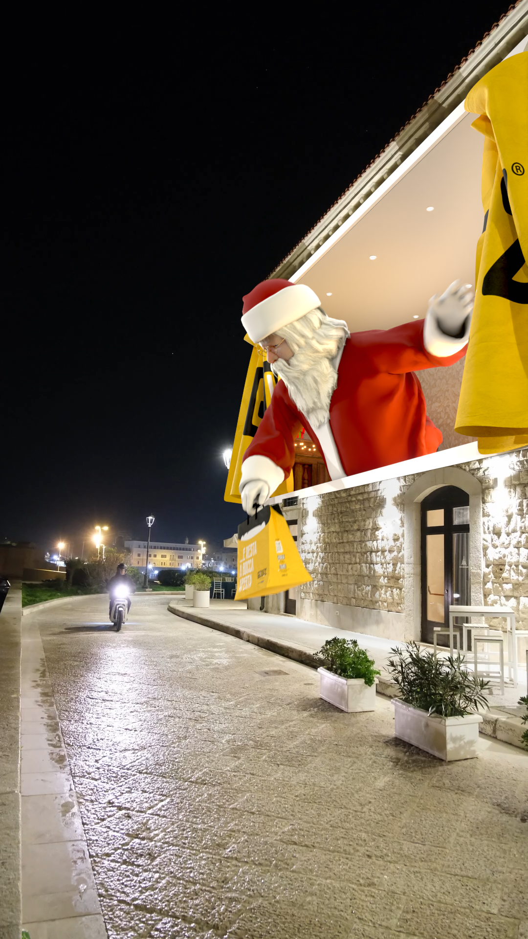 Decorazione natalizia con Babbo Natale gigante che scende da un balcone e tiene una borsa con regali, sulla strada illuminata di sera.