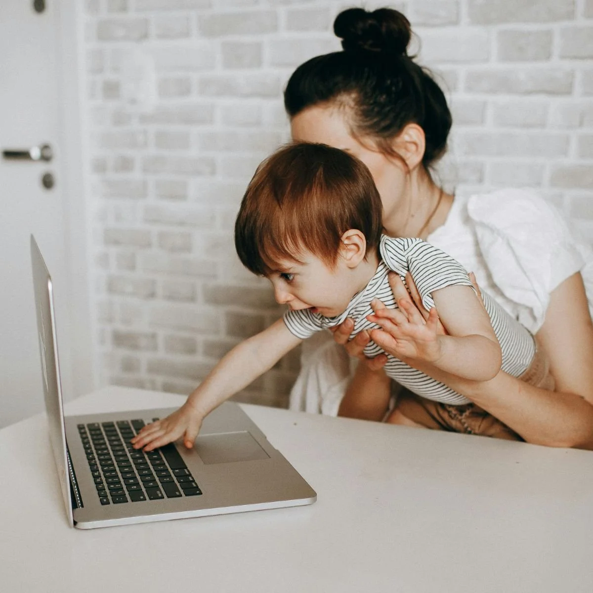 Mom holding a young boy in front of a laptop, both looking at the screen, with the boy reaching out to touch it.