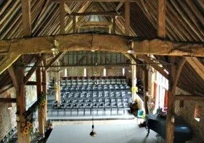 Interior of a rustic barn with wooden beams, overlooking a small auditorium with rows of blue seats.