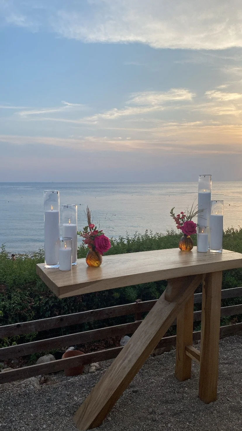 Tall candles on a cake table for a wedding with a sunset ocean view