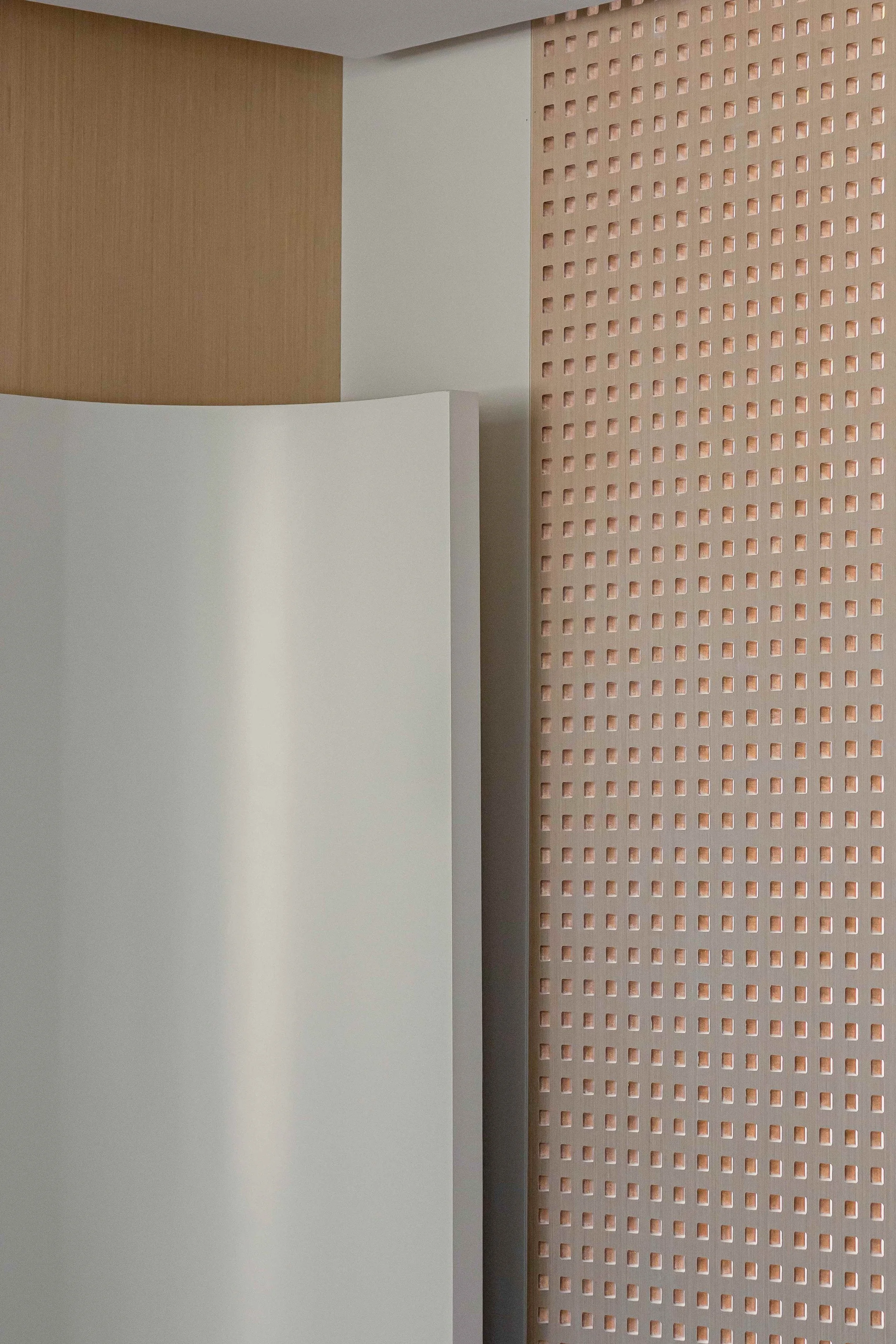 Close-up of a modern interior wall with a curved white panel, a wooden textured section, and a pink perforated panel.