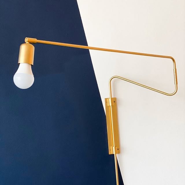 A modern wall lamp with a gold finish, mounted on a wall divided into dark blue and white sections.