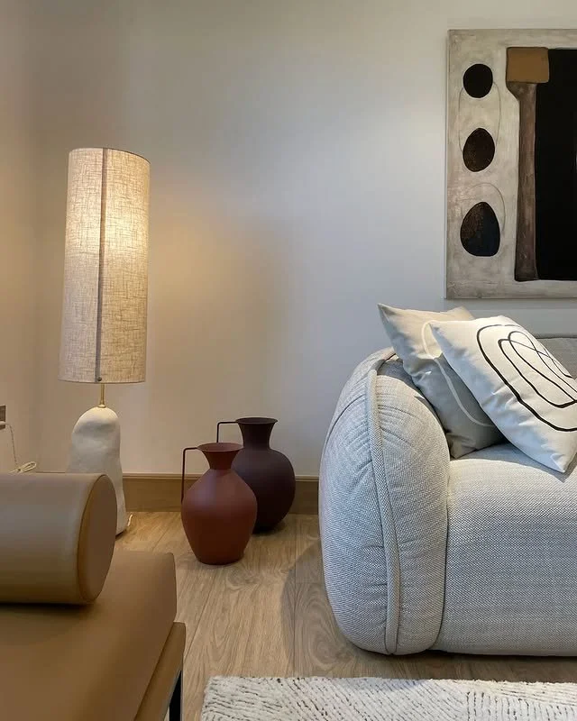 Living room with a beige sofa, black and white pillows, a large abstract wall art, a tall beige lamp, and two decorative vases in the corner.