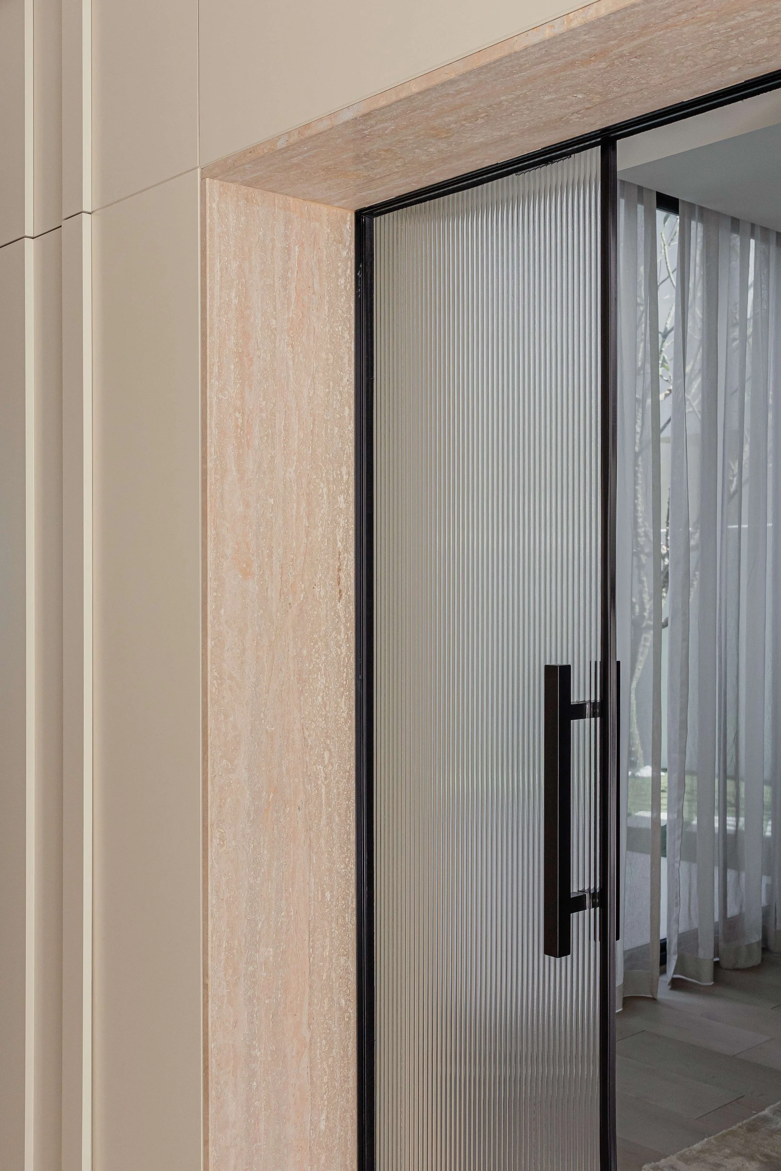 Interior glass door with black handle and black frame, partially open, revealing sheer curtains and windows with trees outside.