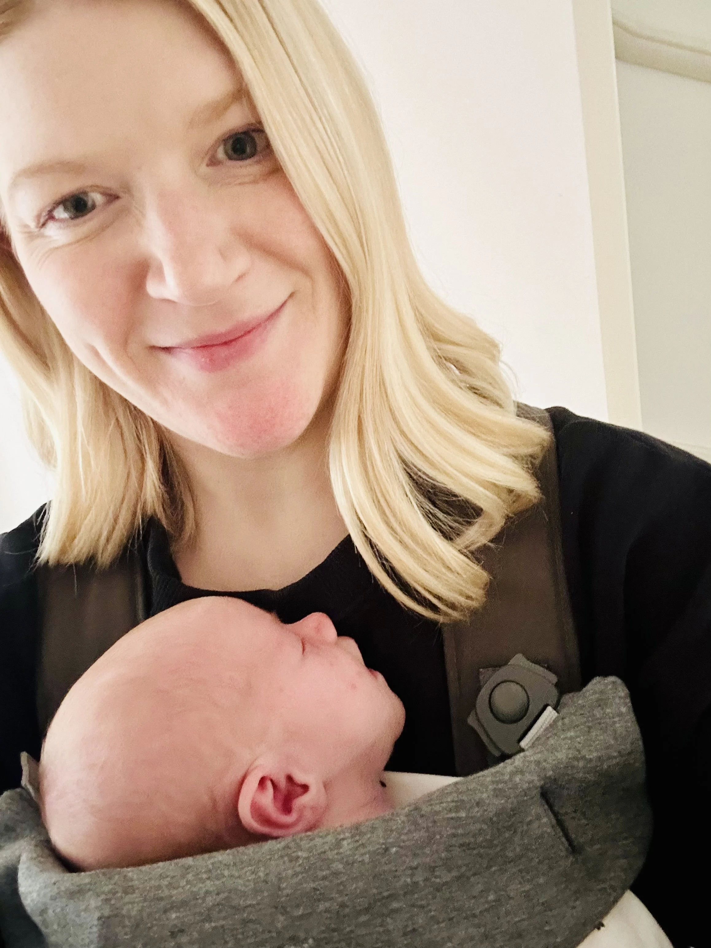 Emily, a certified sleep specialist, wearing her baby in a carrier to illustrate supportive, heart-led parenting