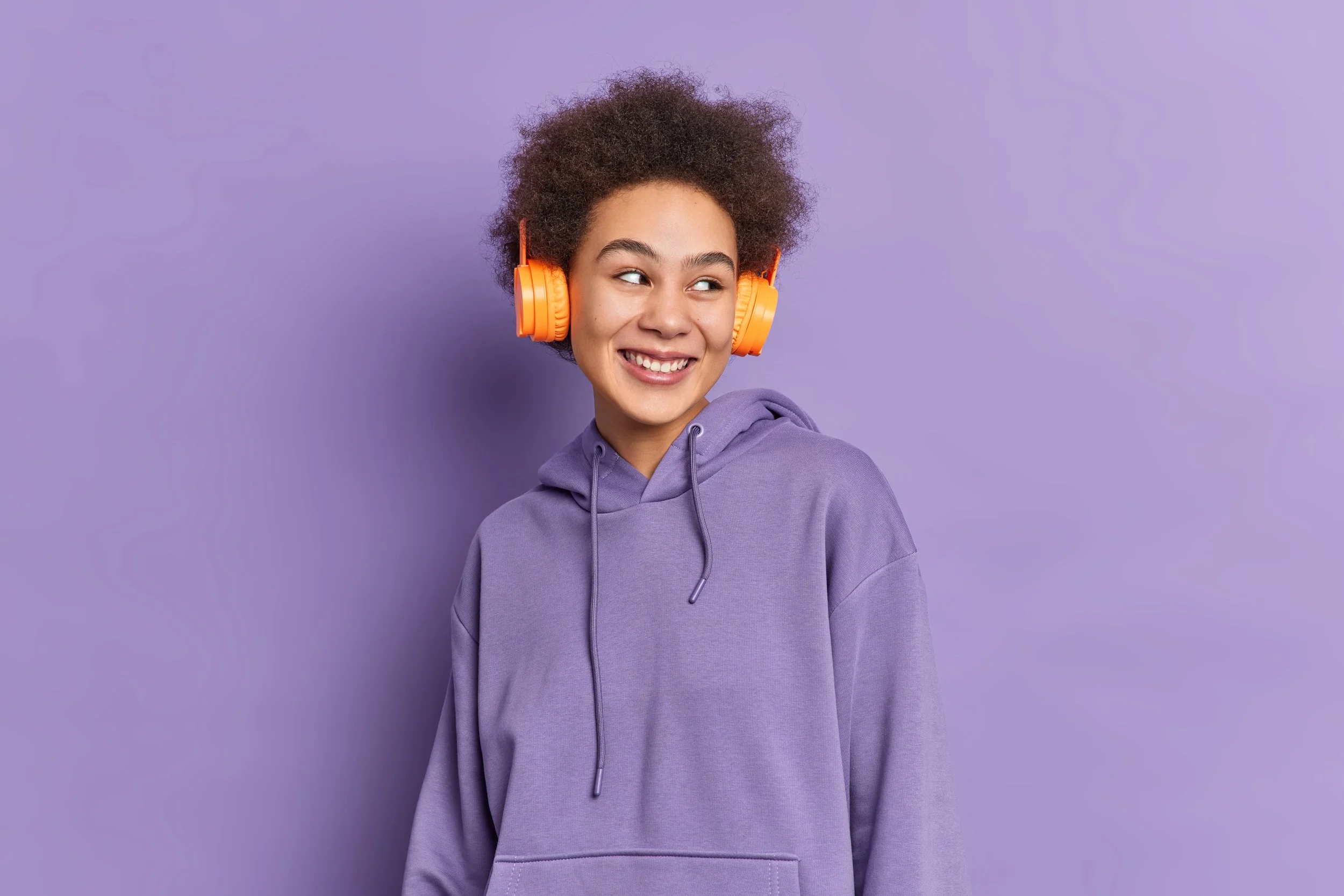 curly-pretty-teenage-girl-wears-stereo-headphones-listens-audio-track-looks-happily-aside-dressed-sweatshirt.jpg