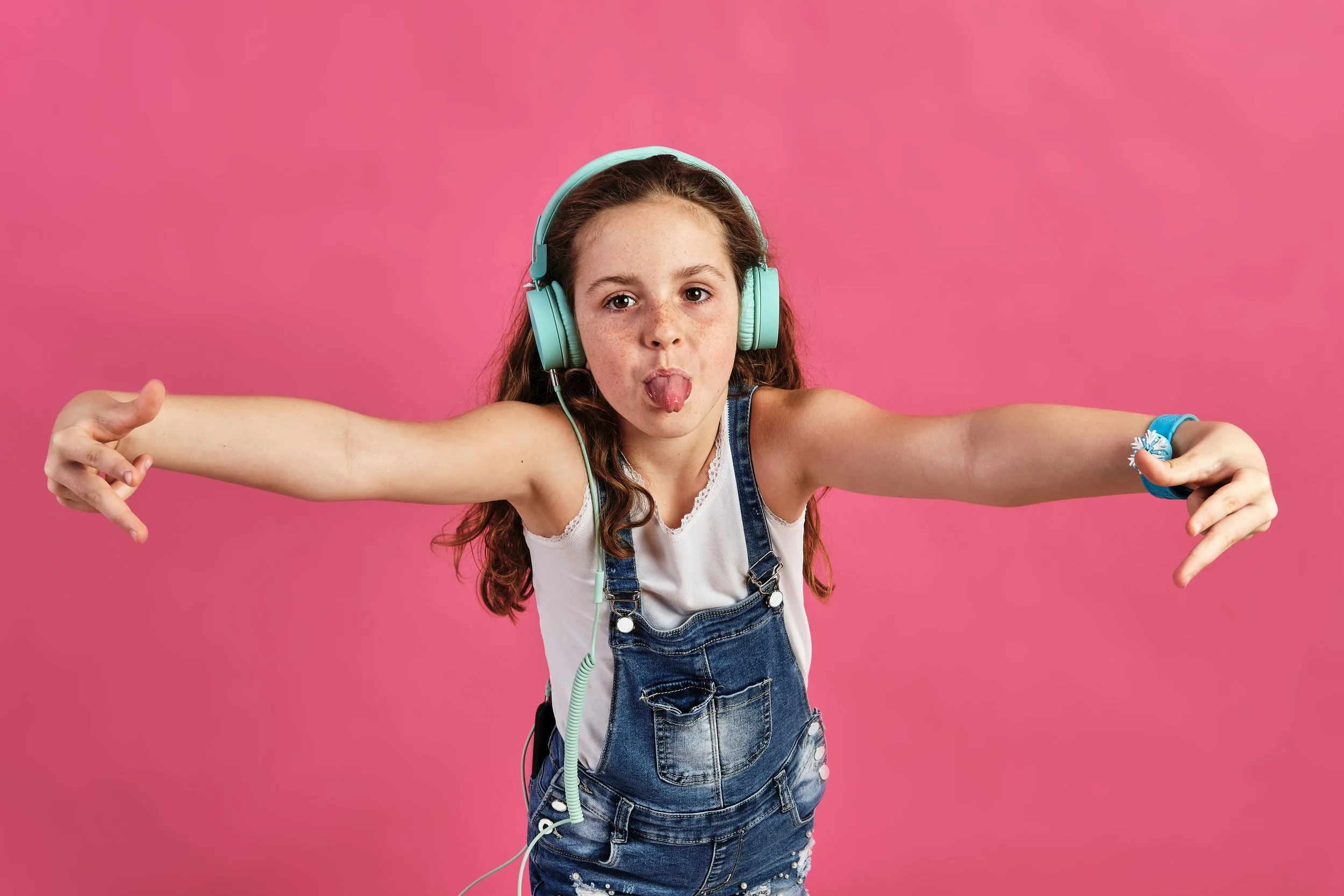 little-girl-posing-with-headphones-with-her-tongue-out-pink-wall.jpg