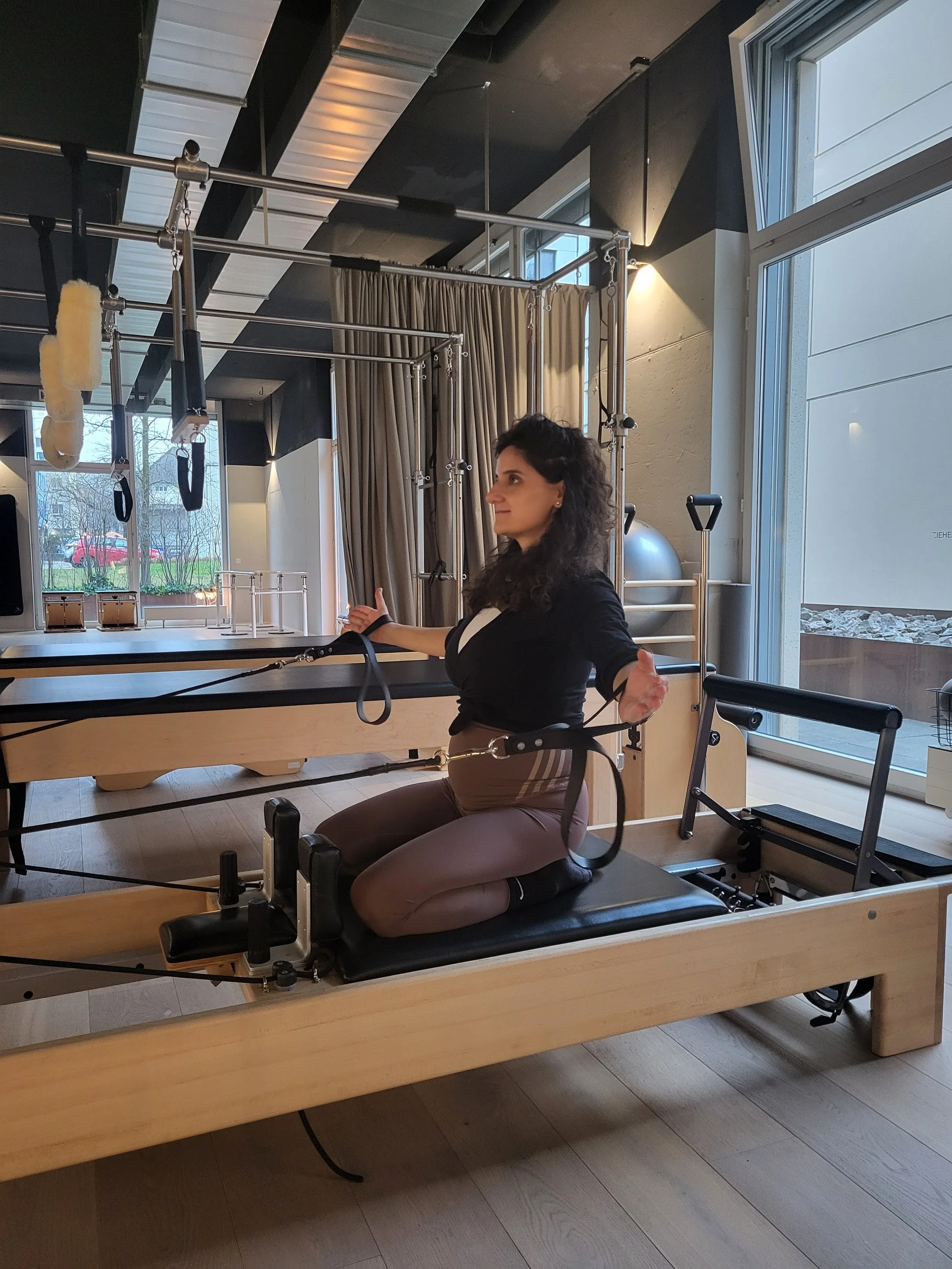 Pregnant woman doing Pilates on a reformer machine in a fitness studio.