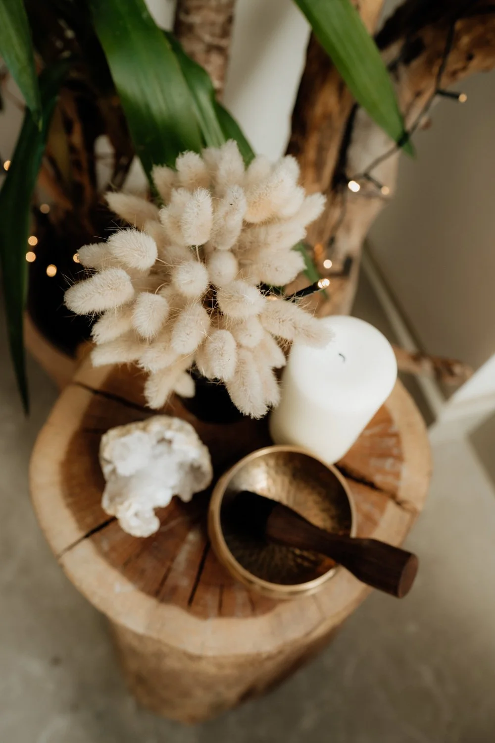 Singing bowl, candle, crystal and dried flowers displayed on tree trunk table
