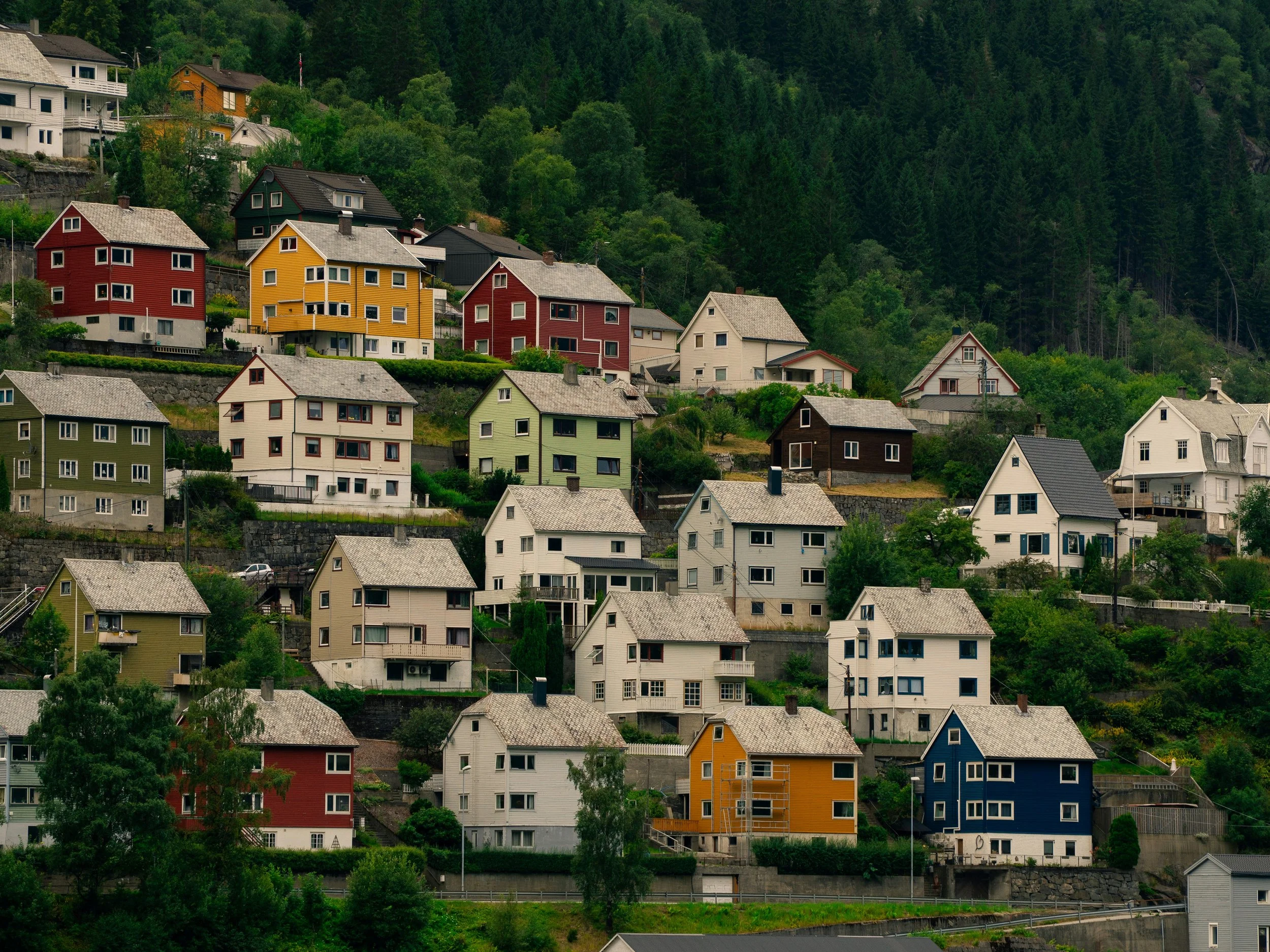 Fargerike hus på en fjellside med trær og grønt landskap i bakgrunnen.