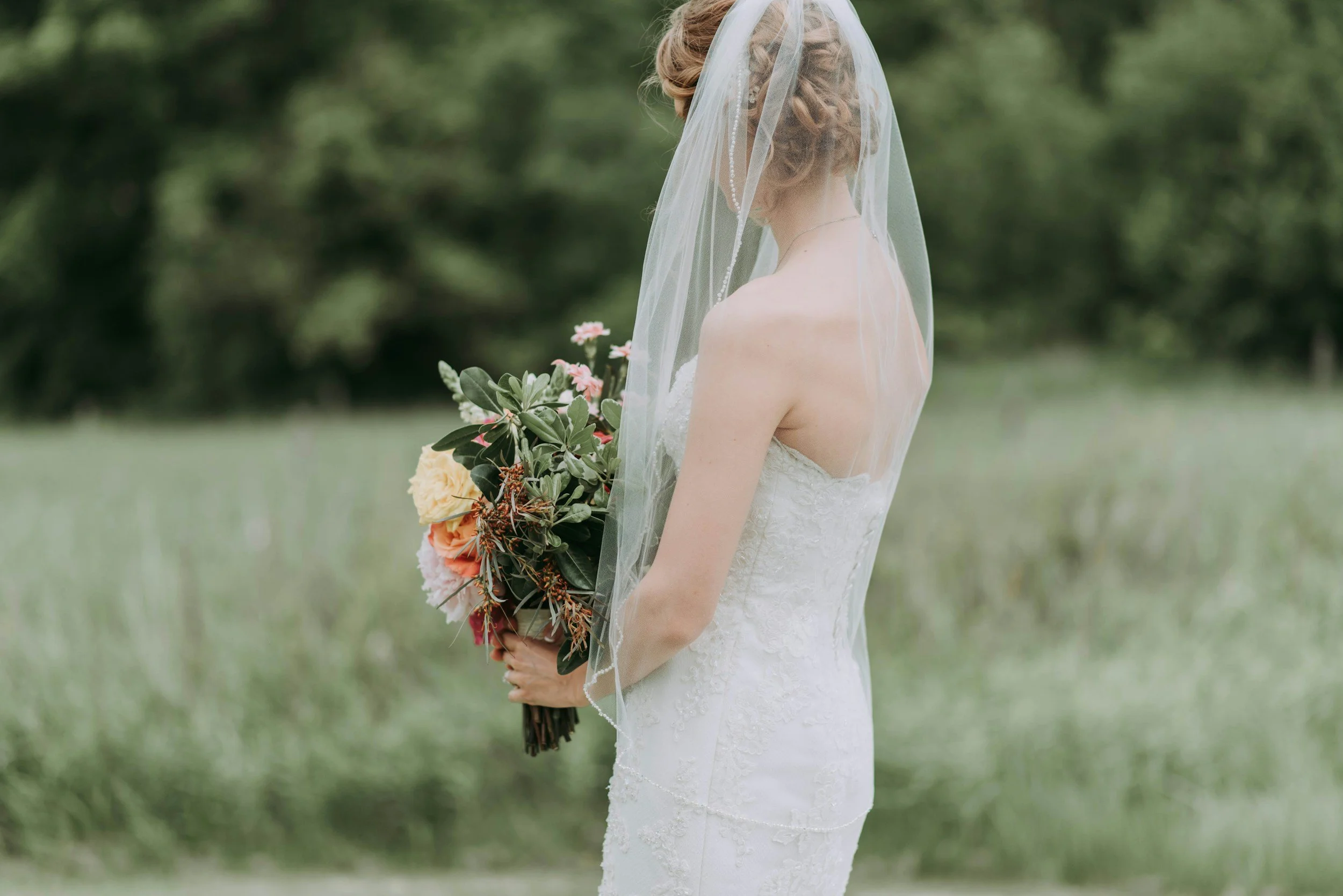 A bride in a white wedding dress holding a bouquet of flowers outdoors.