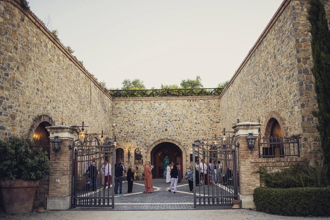 People gathered in a courtyard with stone brick walls and iron gates, inside a historic building with arched doorways and lanterns, during daytime.