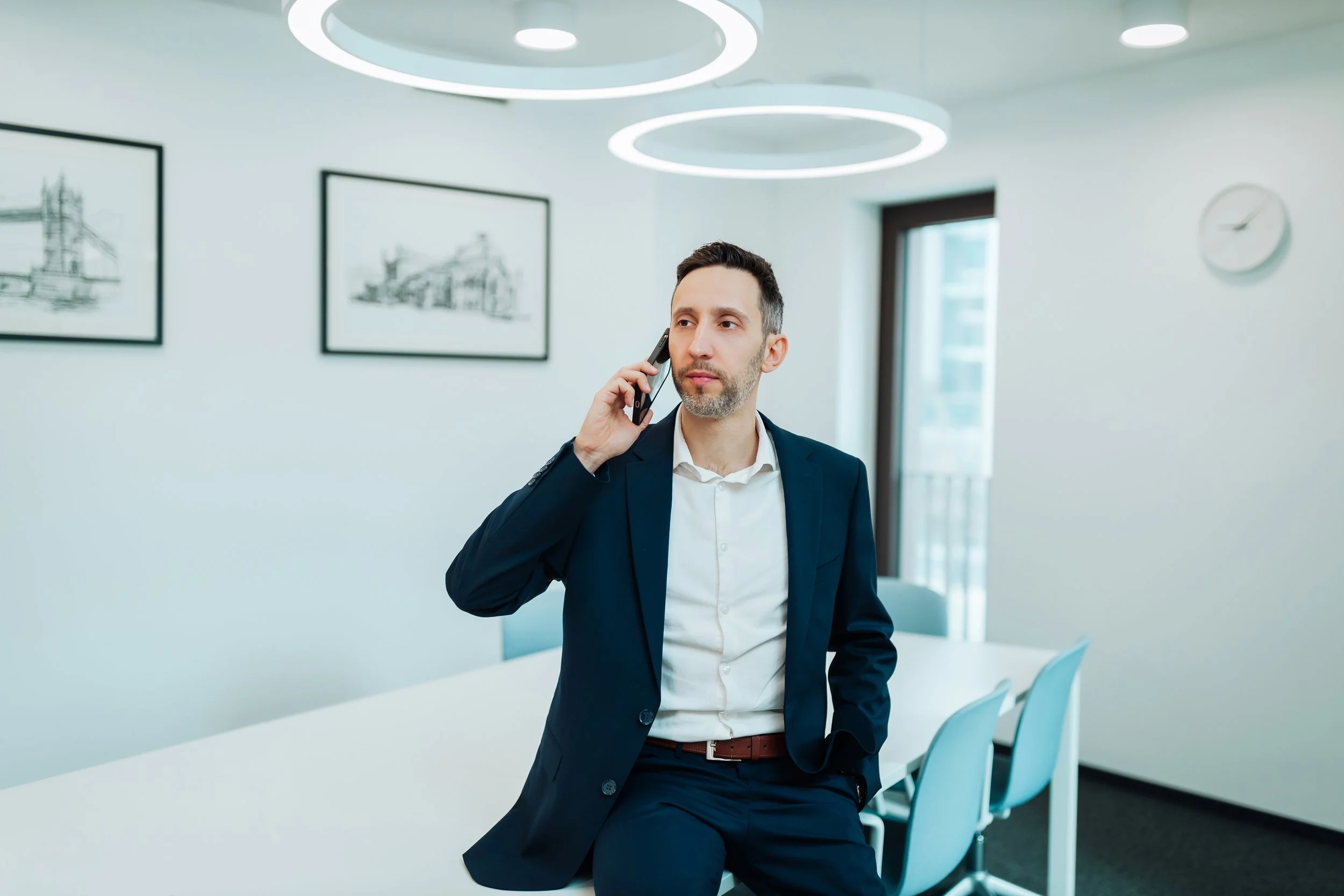 Businessman in a suit talking on the phone in a modern office conference room with minimalist decor.
