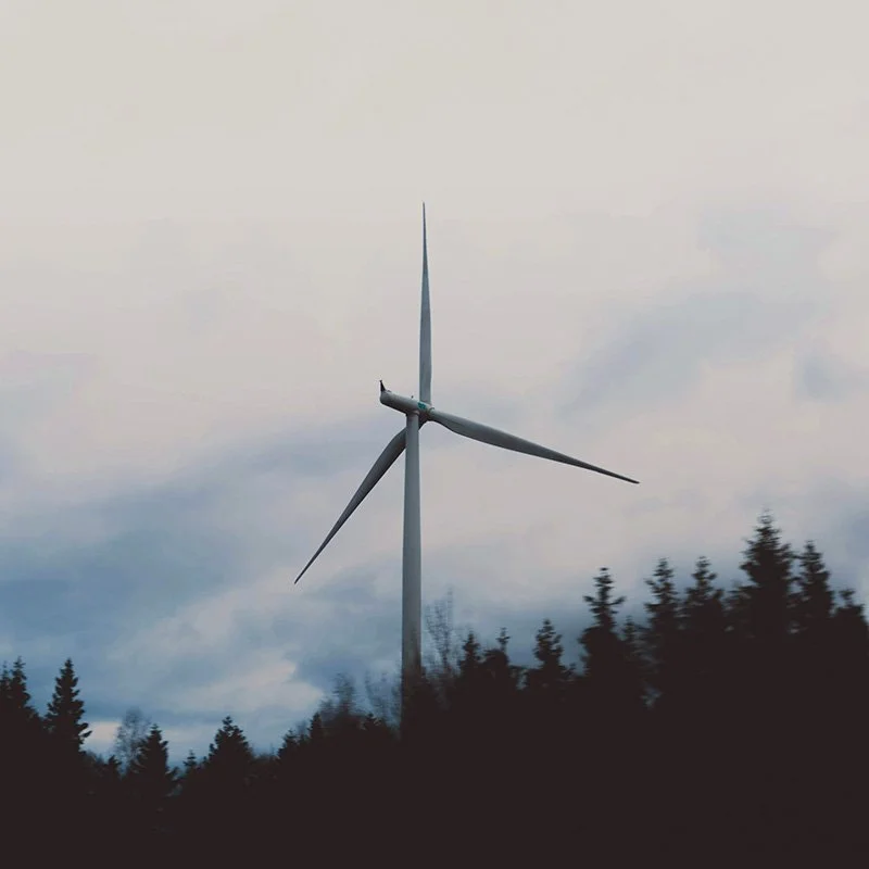 Wind turbine with a backdrop of a forest and clouds