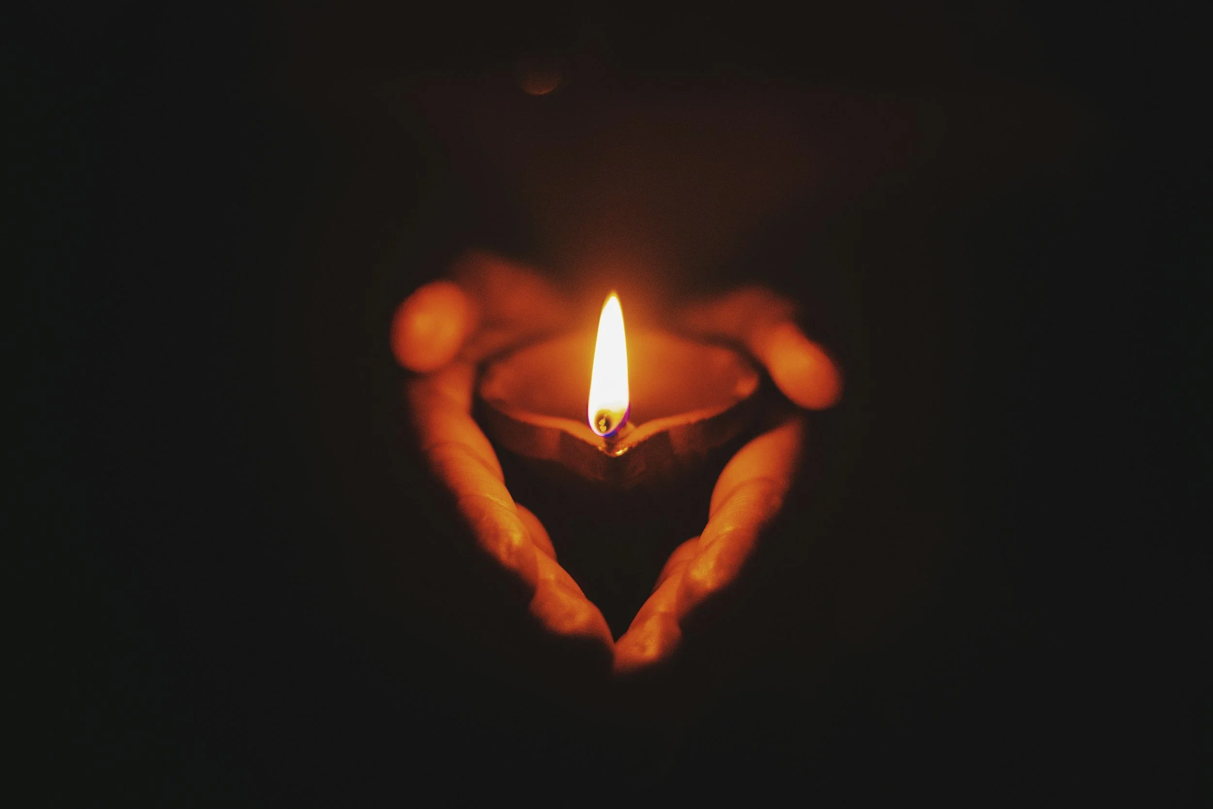 A hand holding a lit candle in a small holder, with a dark background.