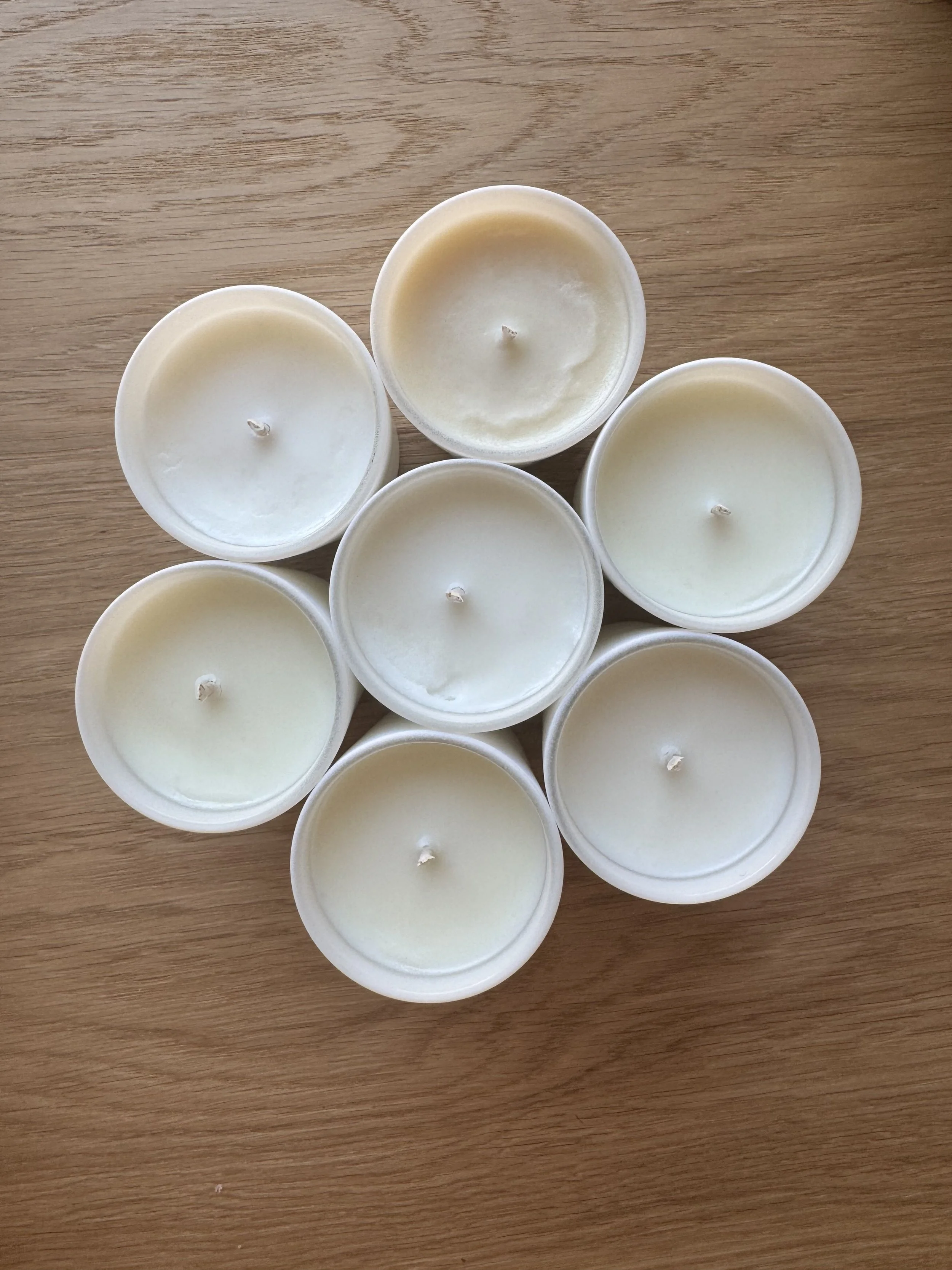 Top view of seven white candles on a wooden surface arranged in a circular pattern.
