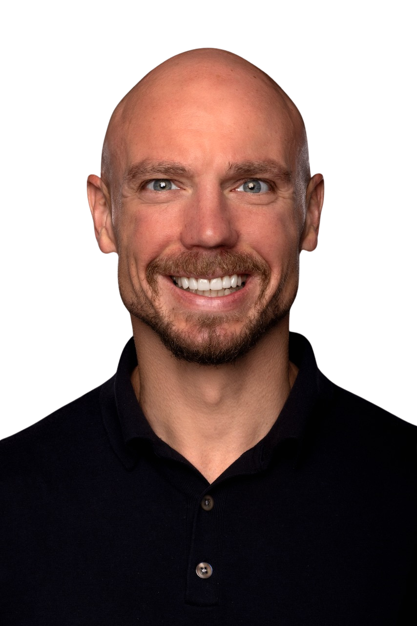 Ein Mann mit einem lichten Bart und blauen Augen, der ein schwarzes Hemd trägt, lächelt vor dunklem Hintergrund.