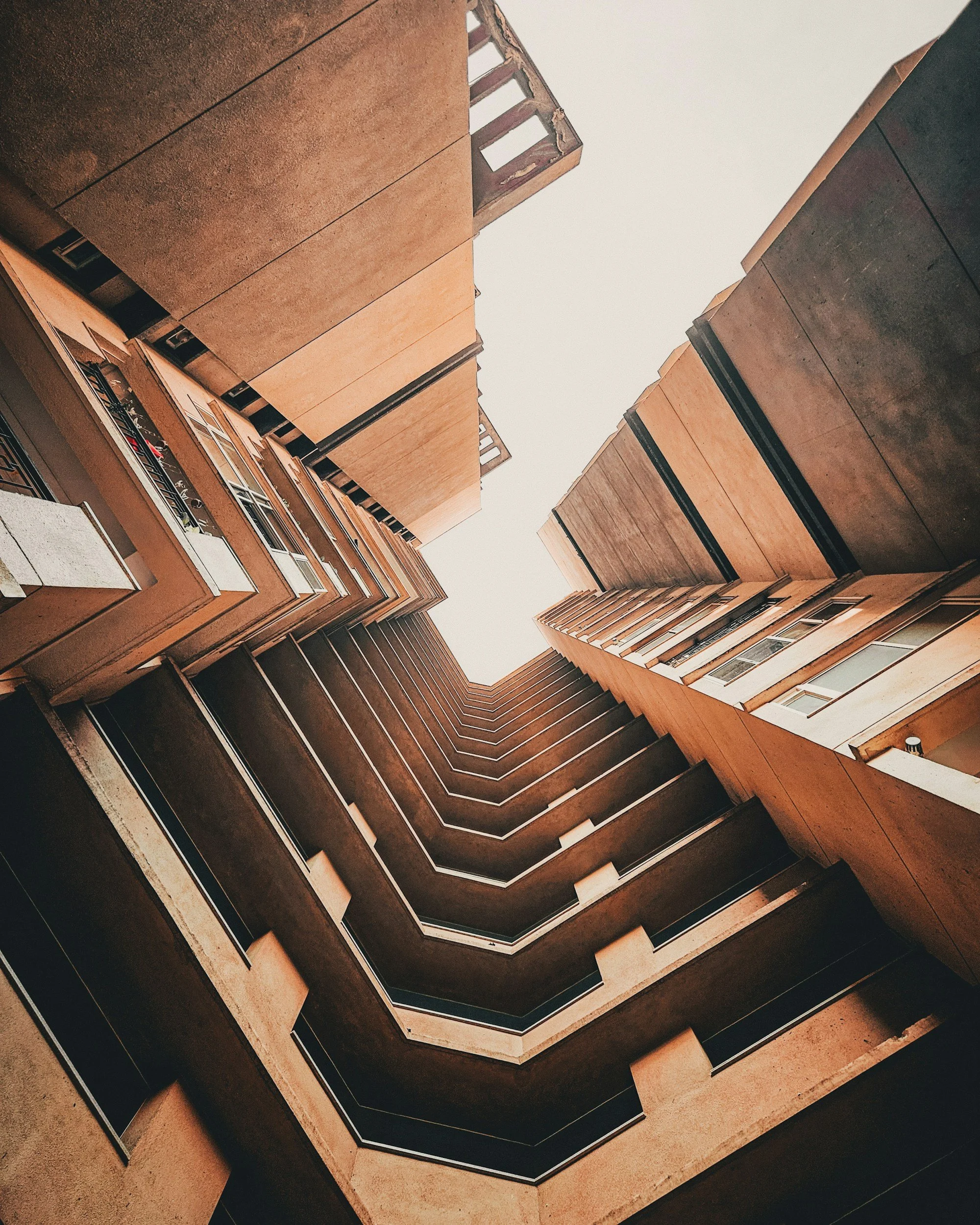 Looking up at the interior of a tall, multi-story apartment building with a glass ceiling at the top.