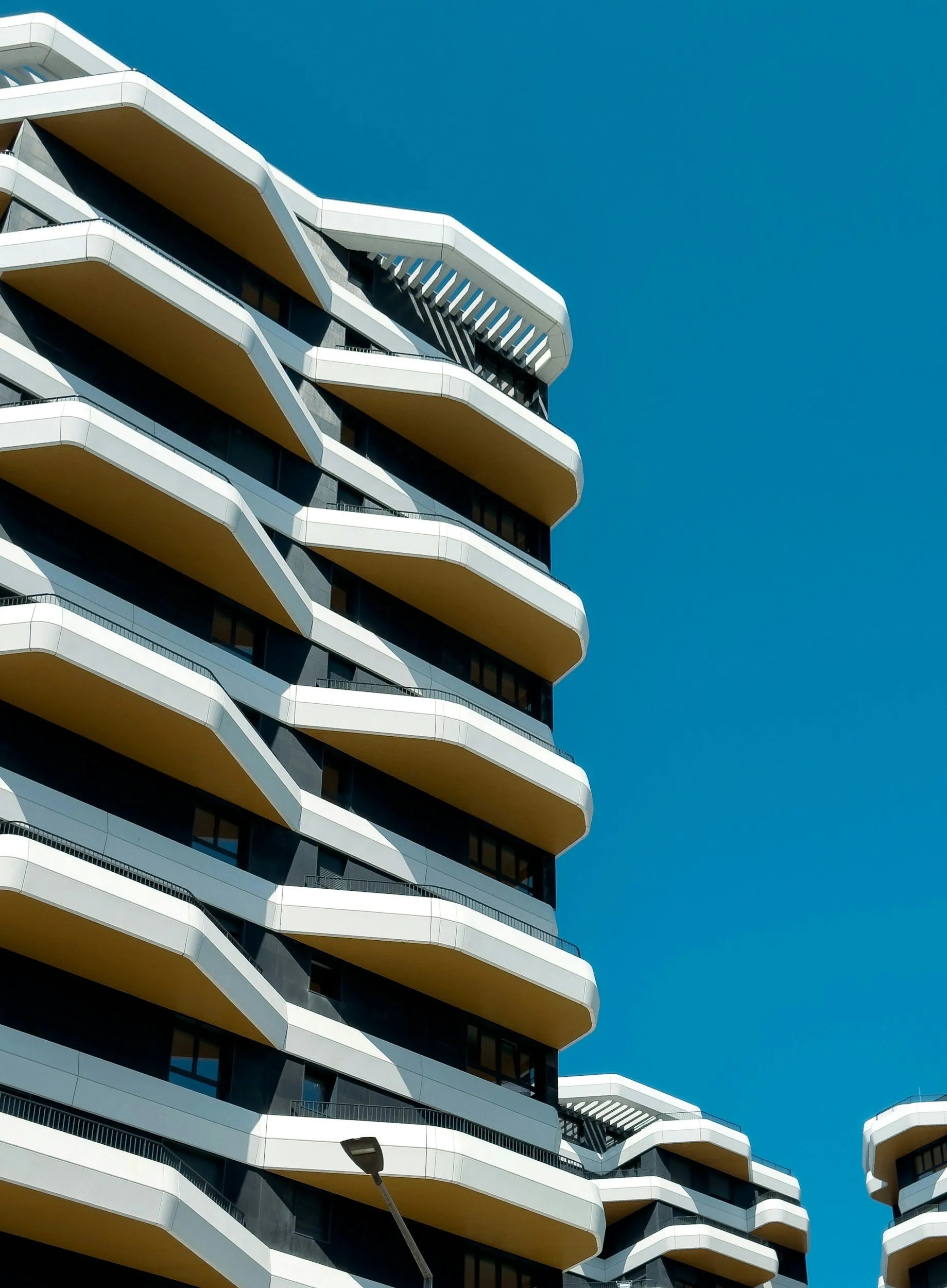 Modern multi-story building with unique, curved balconies against a clear blue sky.