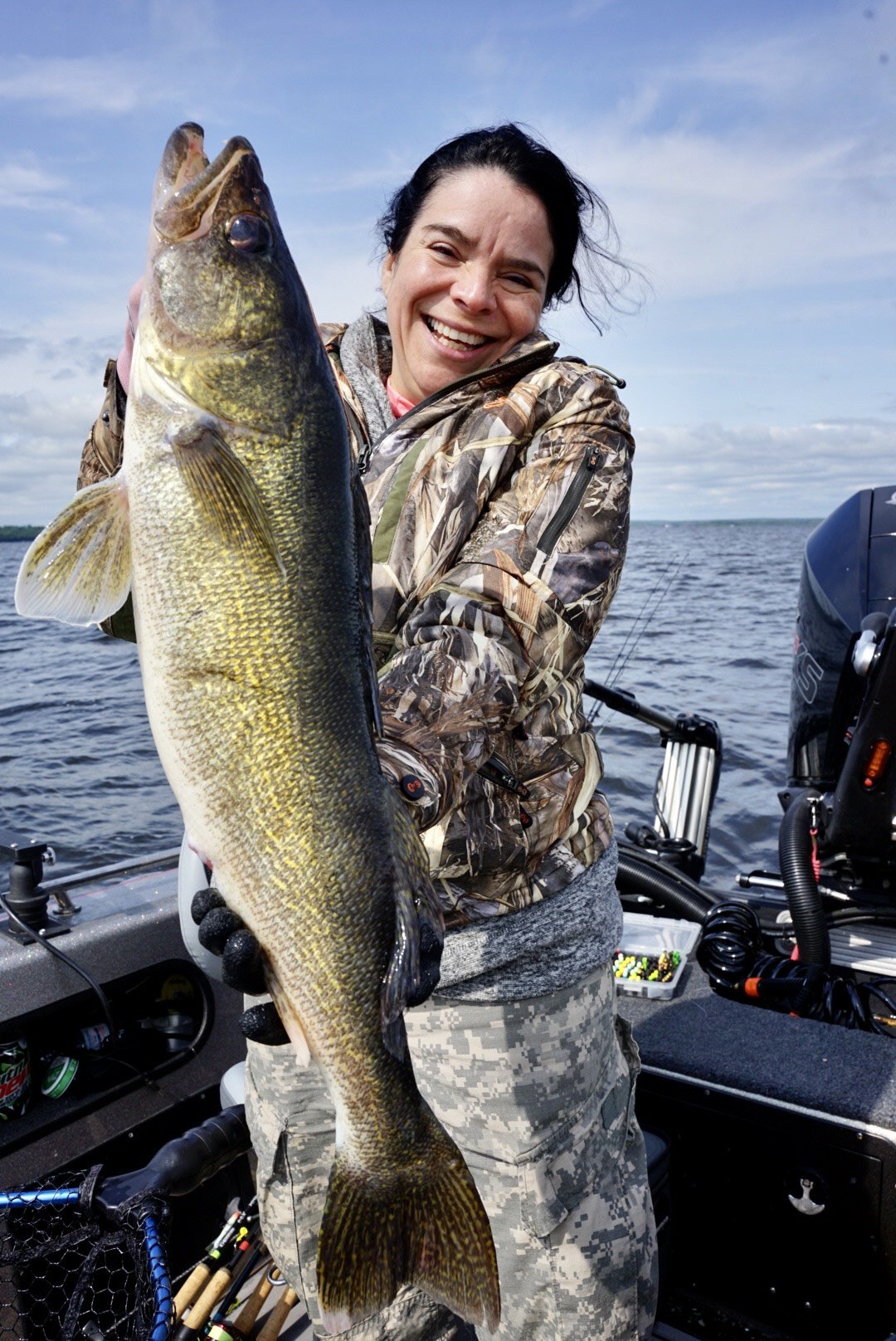 Woman holding a large fish on a boat in open water, smiling at the camera during daytime.