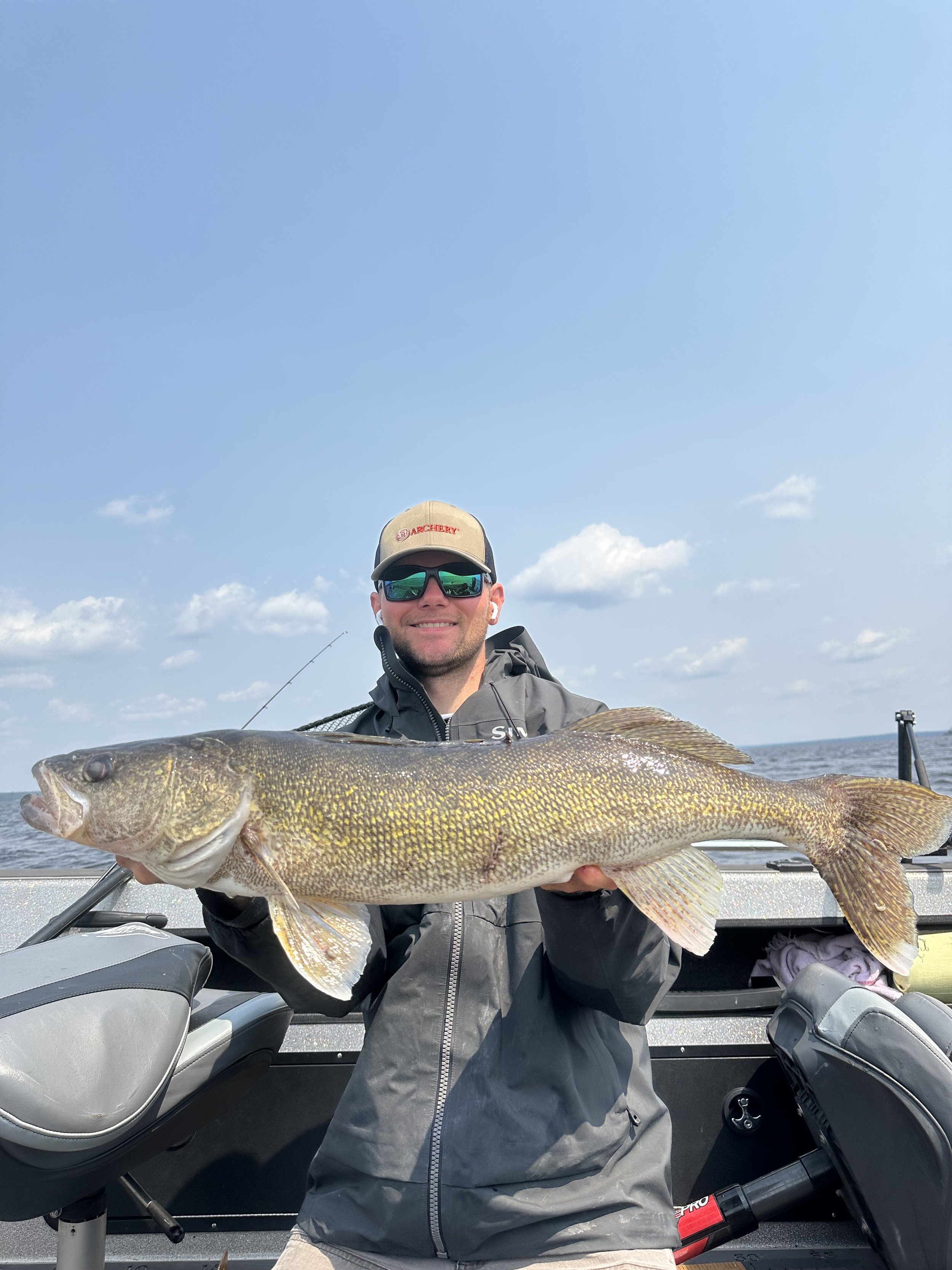 Man holding a large fish on a boat with water and sky in the background.