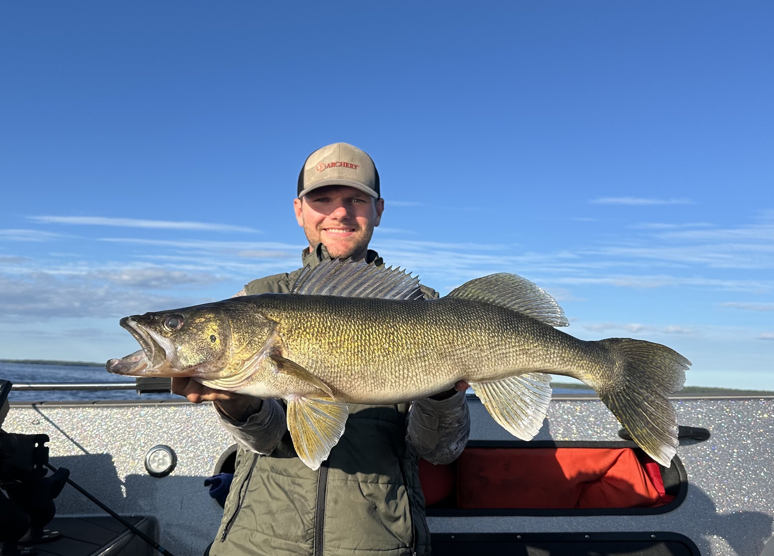 A man holding a large fish on a boat, with water and sky in the background.