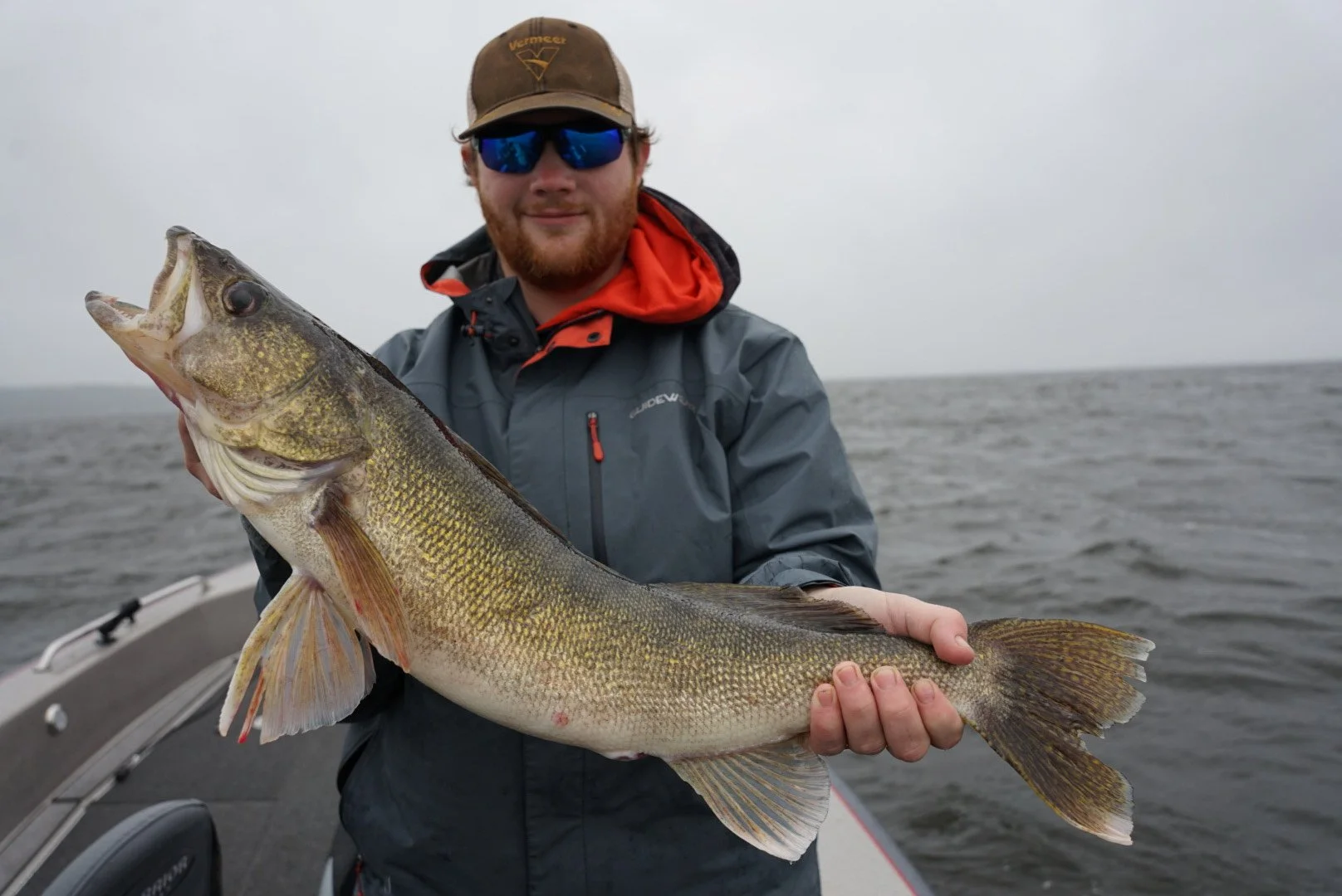 Man in raincoat and sunglasses holding a large fish on a boat in open water