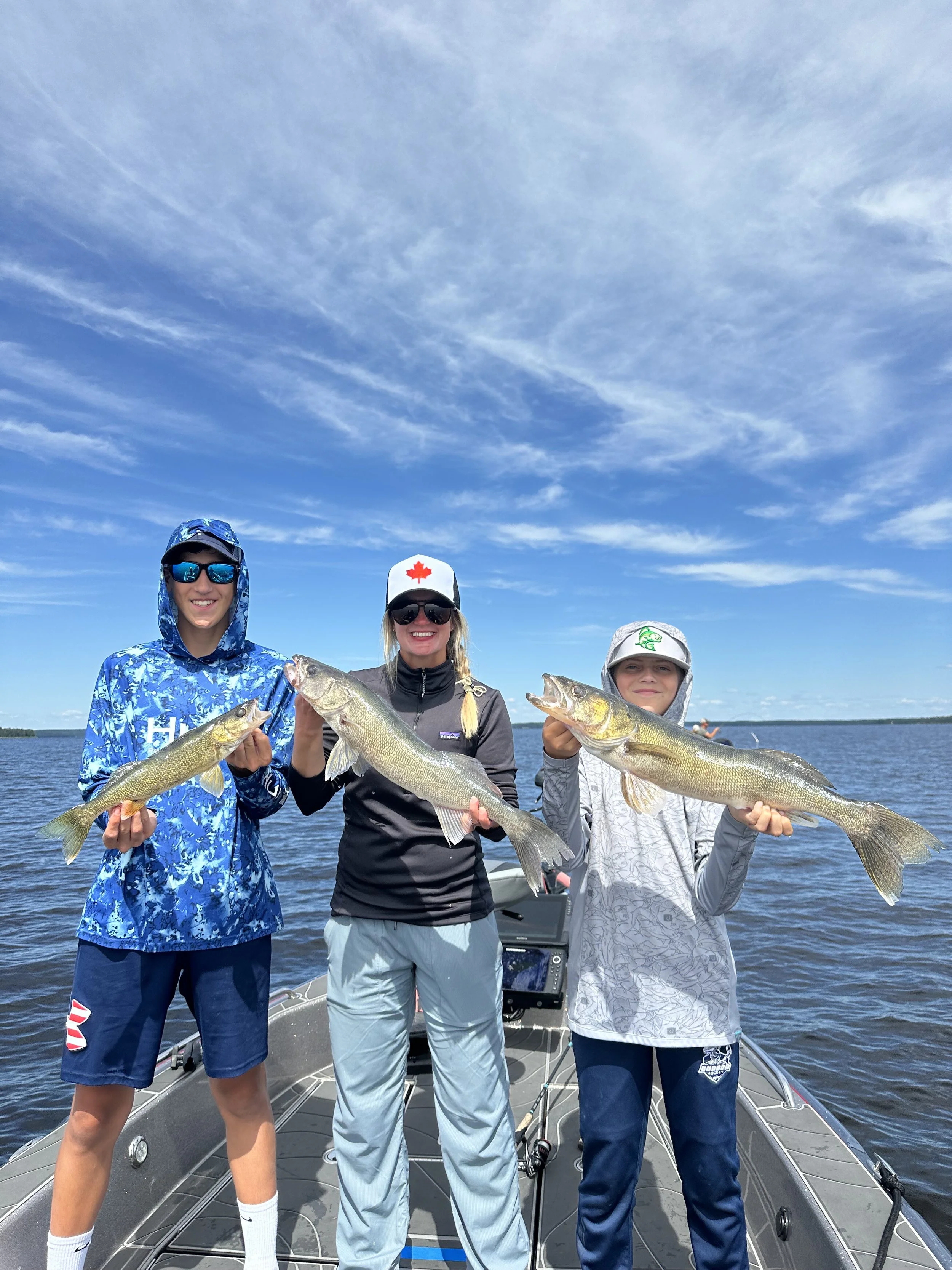 Three people standing on a boat holding fish they caught, with blue sky and water in the background.