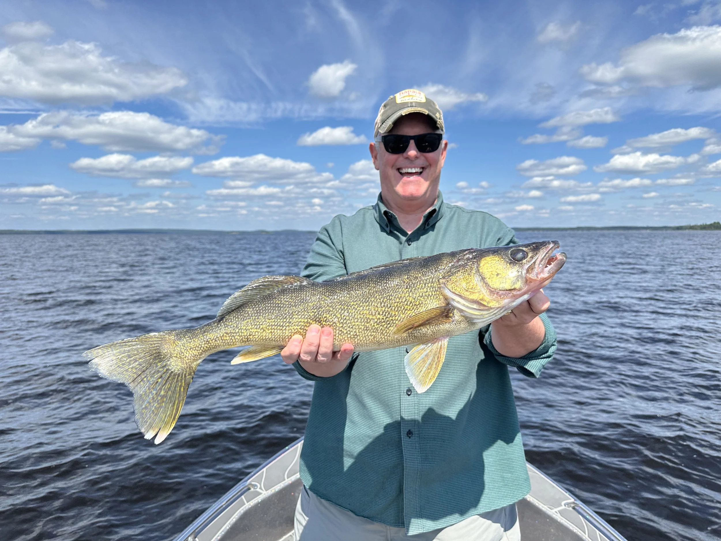 Man in sunglasses and green shirt holding a large fish on boat in lake.