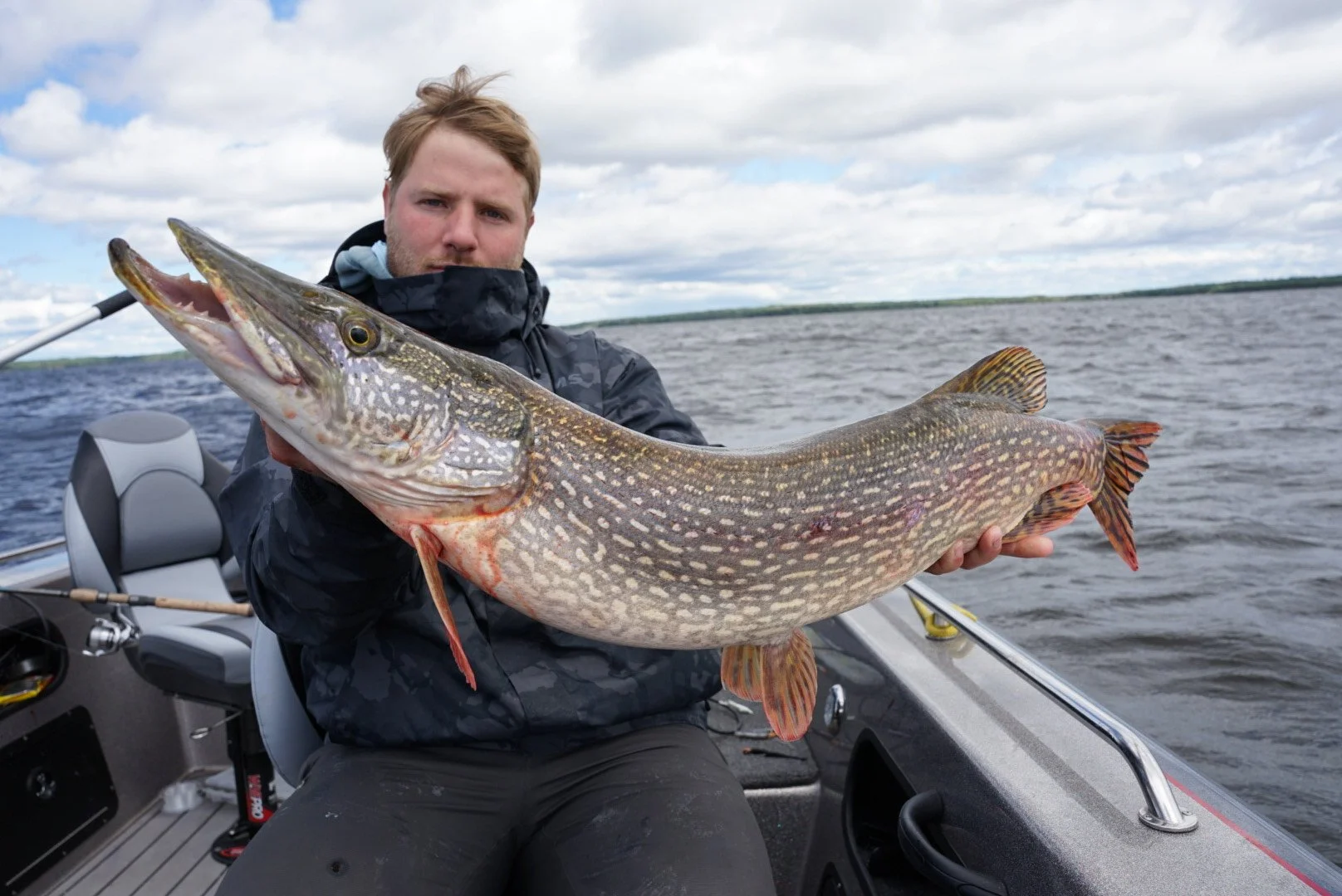 Man on boat holding large fish in open water under cloudy sky.