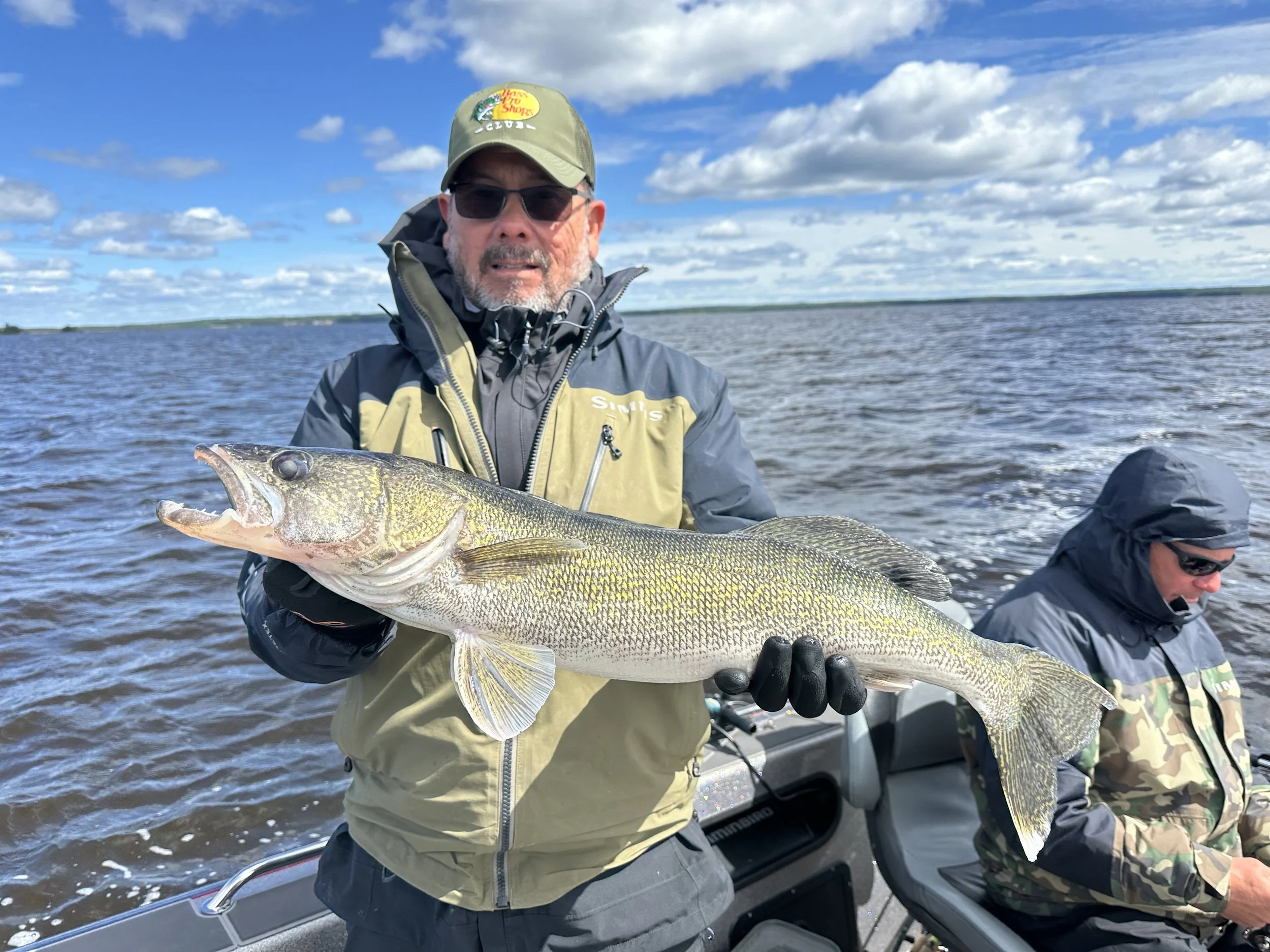 A man holding a large fish on a boat during the day, with another person sitting next to him.