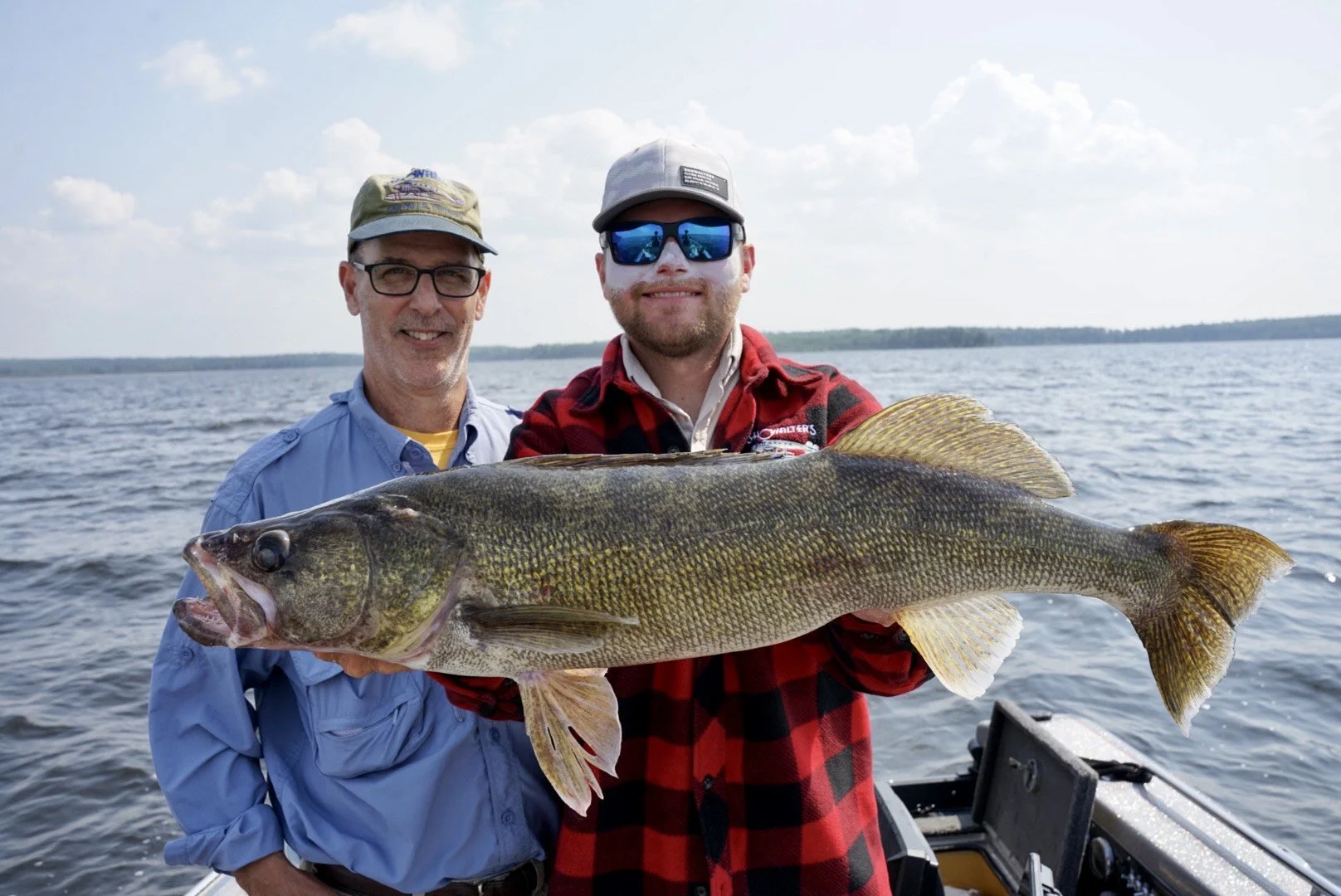 Two men on a boat holding a large fish with water and sky in the background.