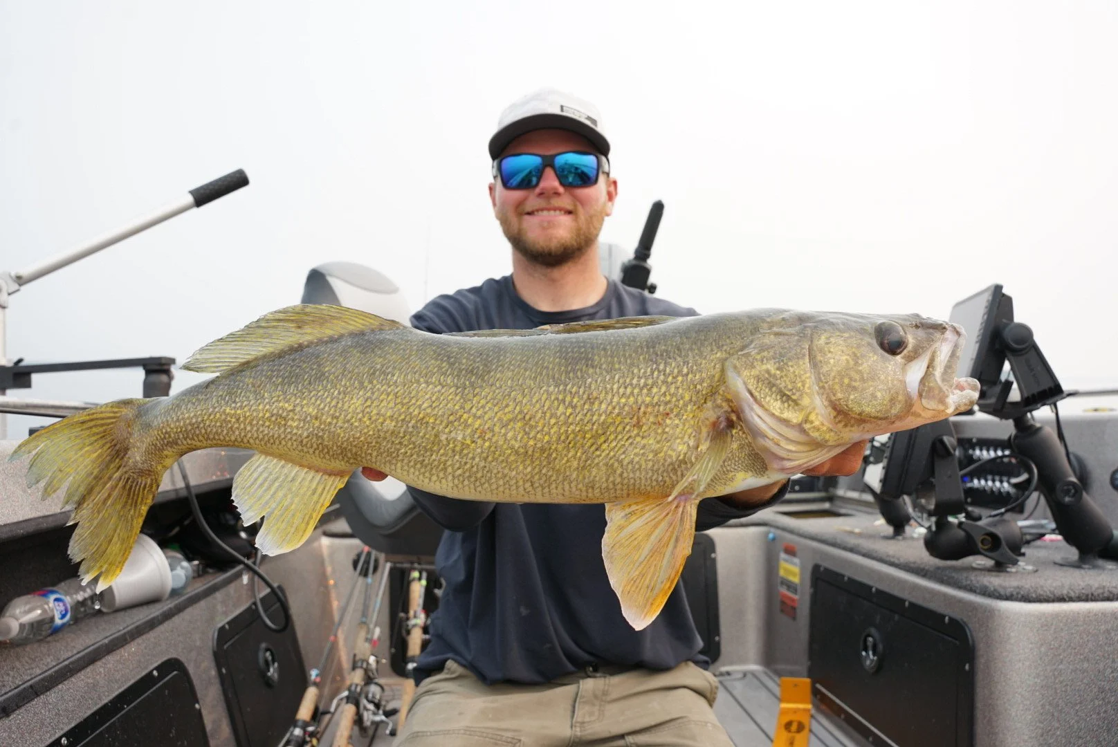 A man in sunglasses holding a large fish on a boat.