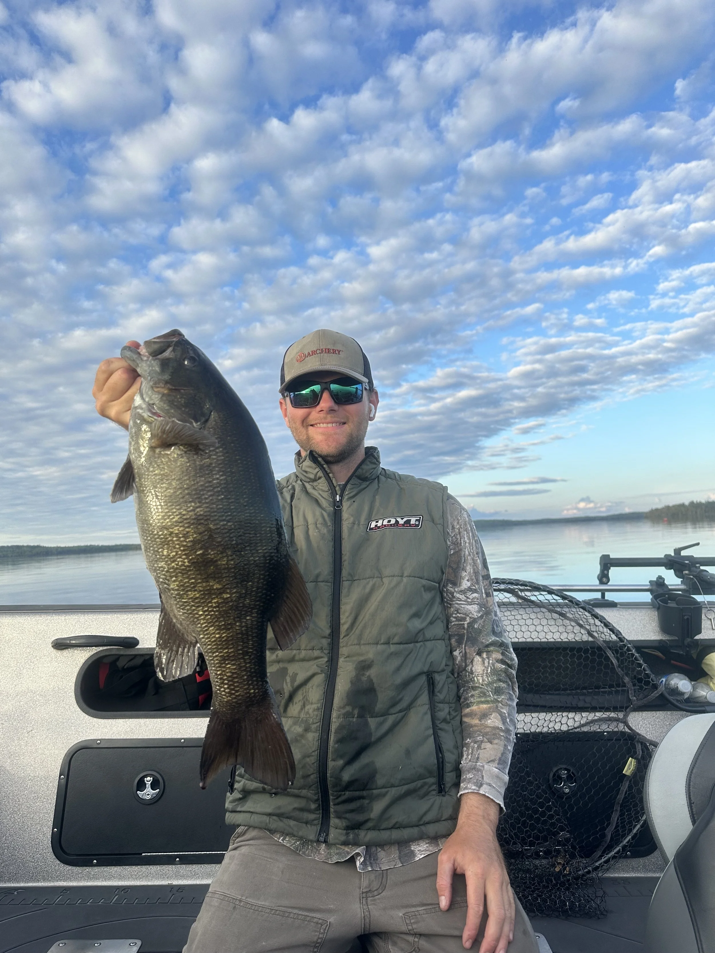 Man holding a large fish on a boat with water and sky in the background.