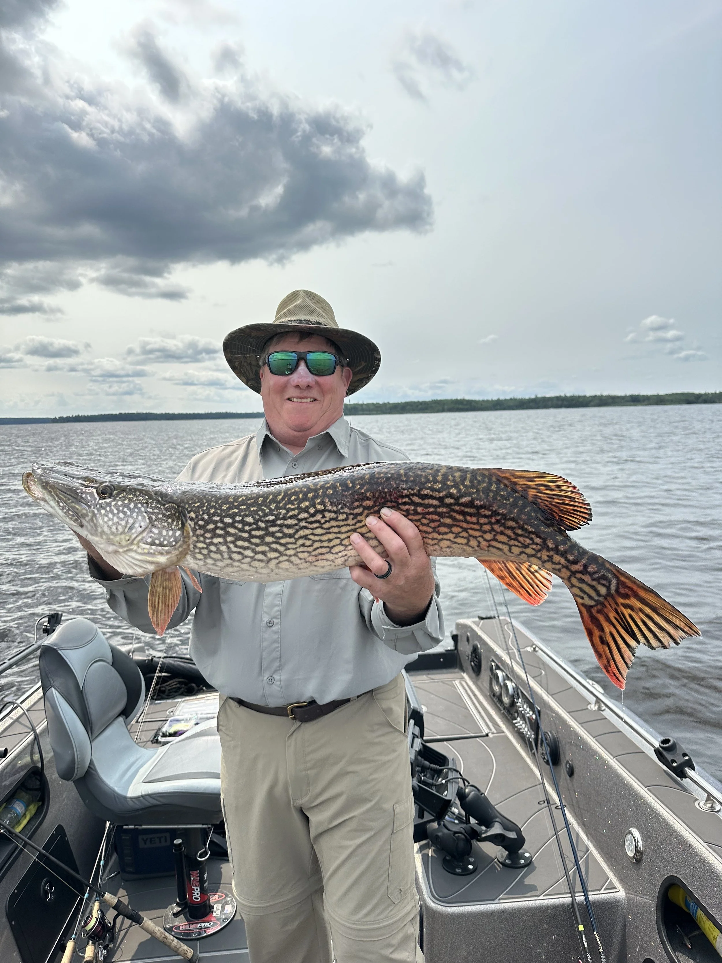 A man holding a large fish on a boat with water and cloudy sky in the background.