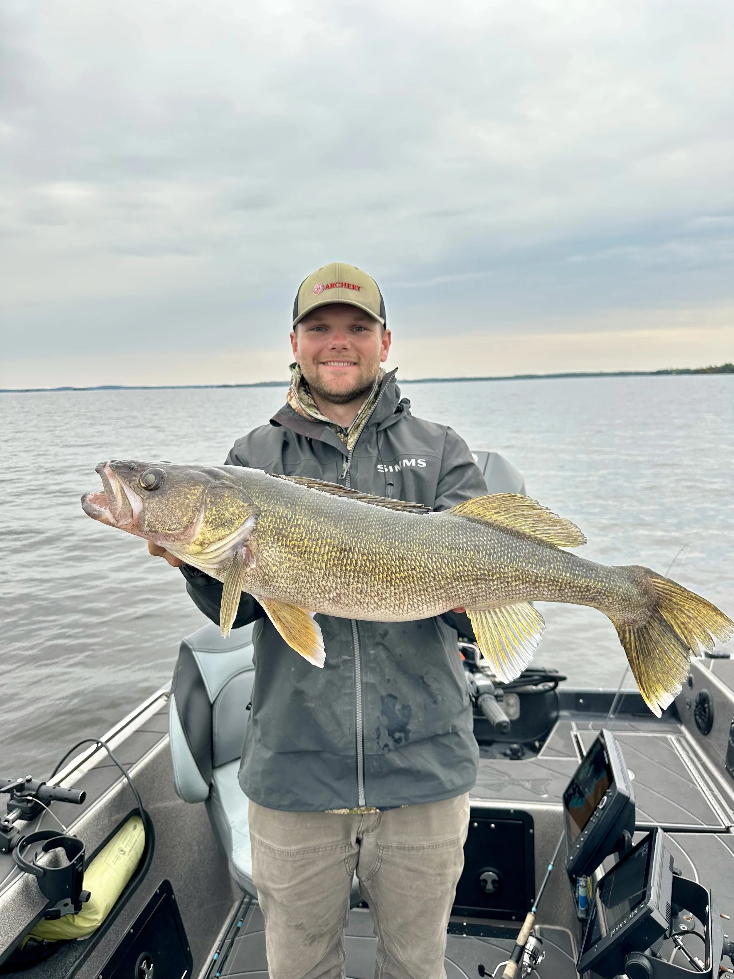 A man on a boat holding a large fish, with gray water and cloudy sky in the background.
