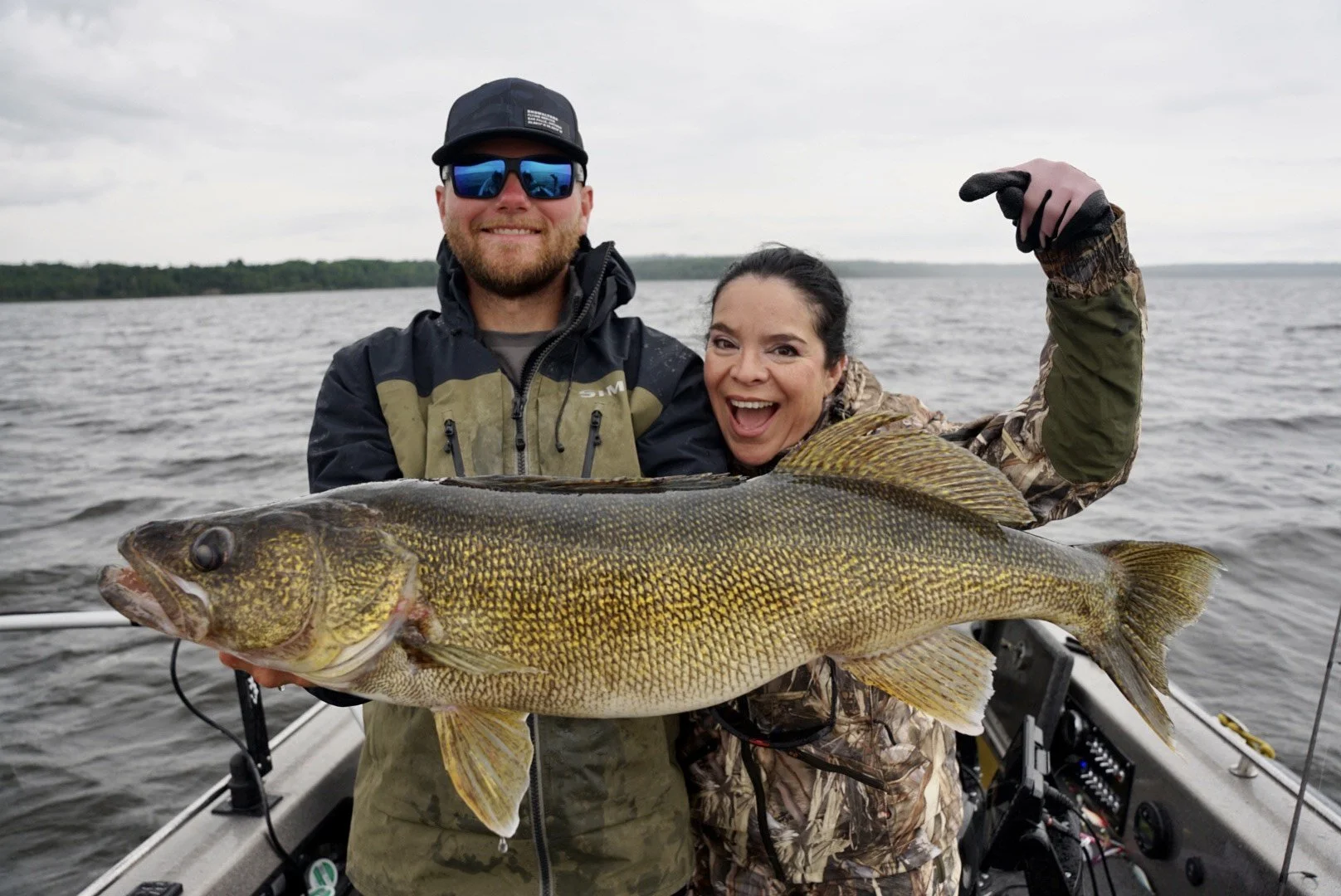 Two people on a boat holding a large fish, smiling at the camera