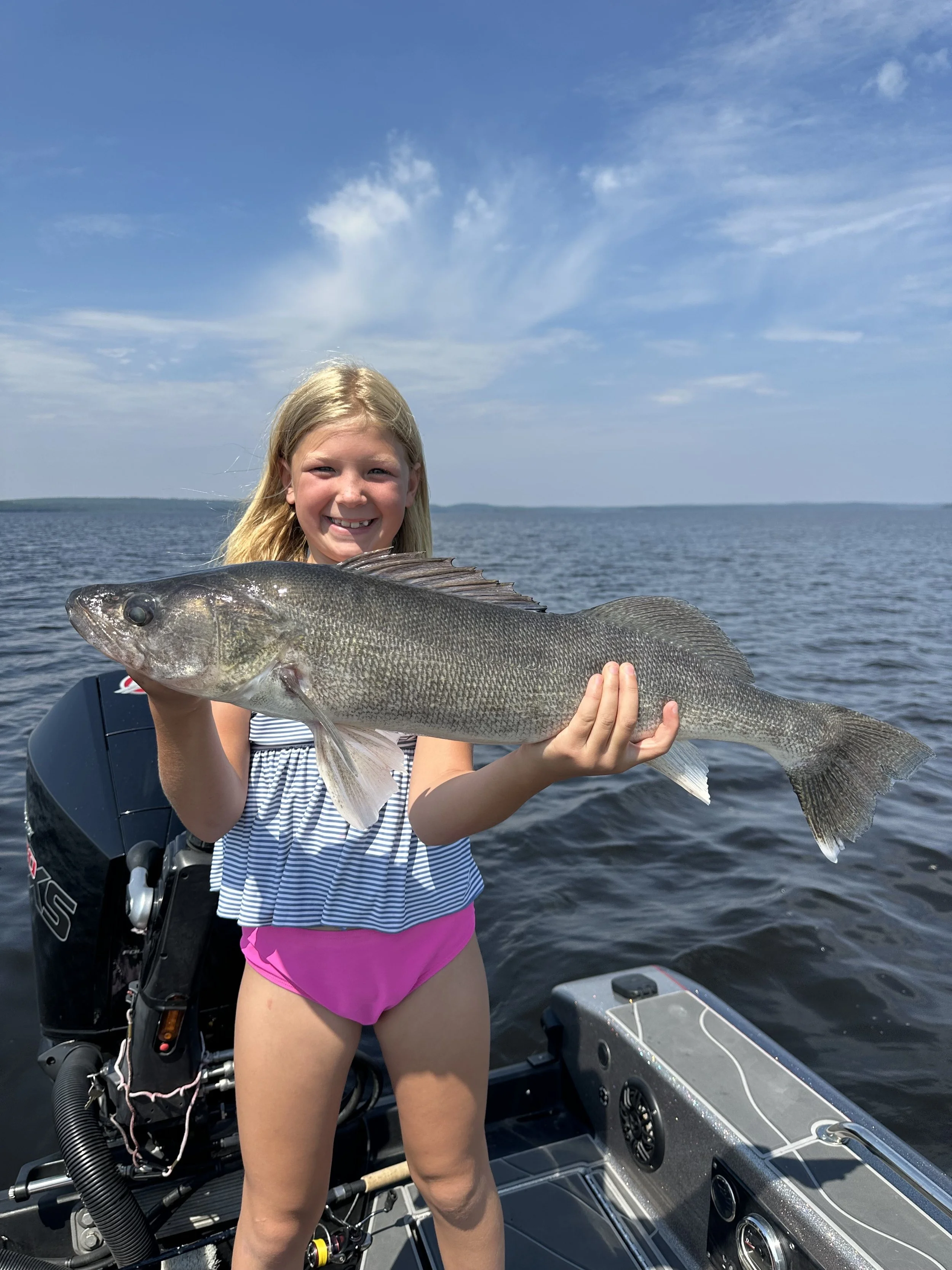 Young girl holding a large fish on a boat with open water and blue sky in the background.