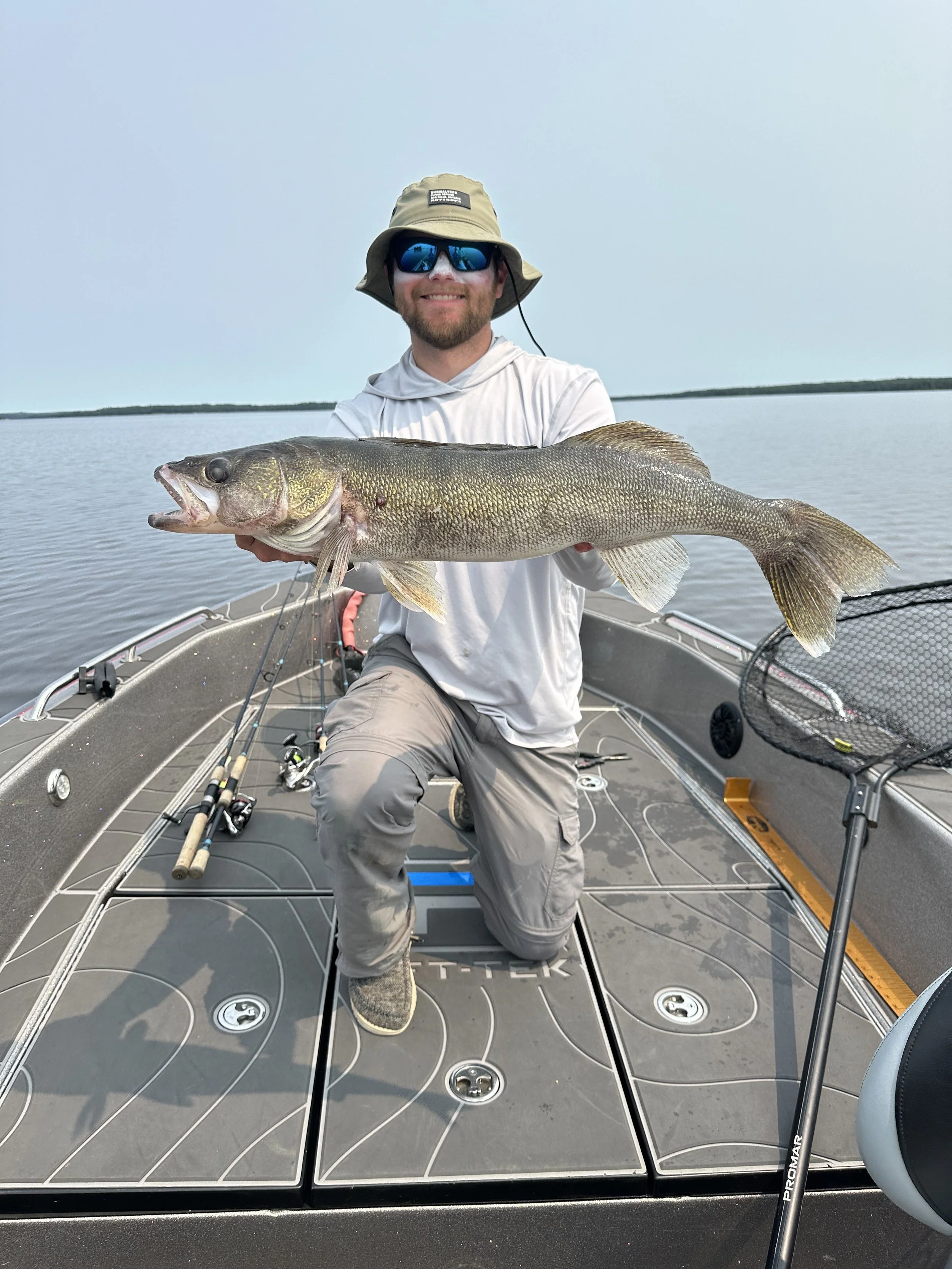 Man holding a large fish on a boat in a lake with calm water and a cloudy sky.