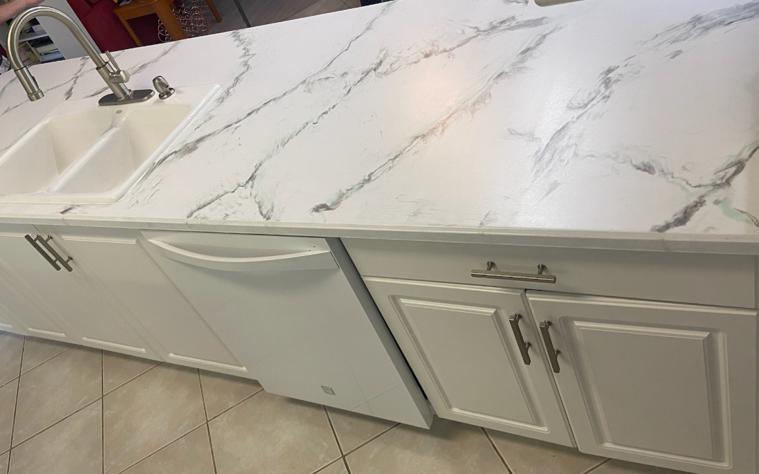 Kitchen countertop with a white marble pattern, white cabinets, a kitchen sink with a chrome faucet, and beige tiled floor.