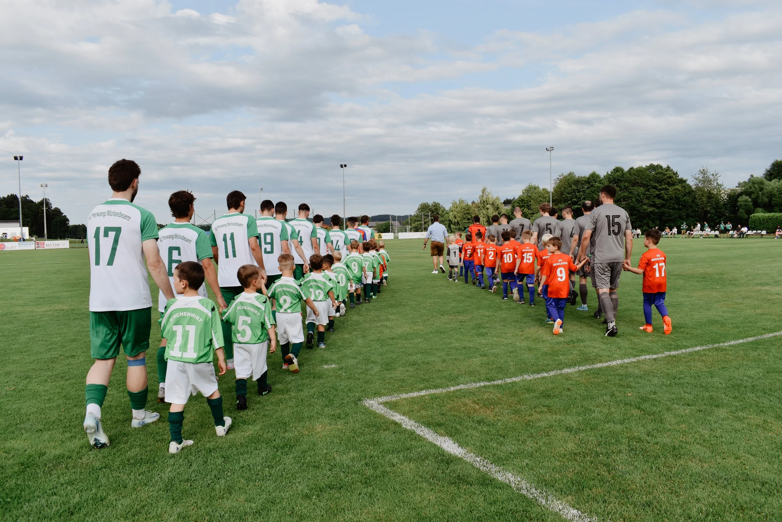 Jugendfußballmannschaften in grüner und orangefarbener Kleidung laufen auf einem Fußballplatz in einer Reihe vor einem Spiel